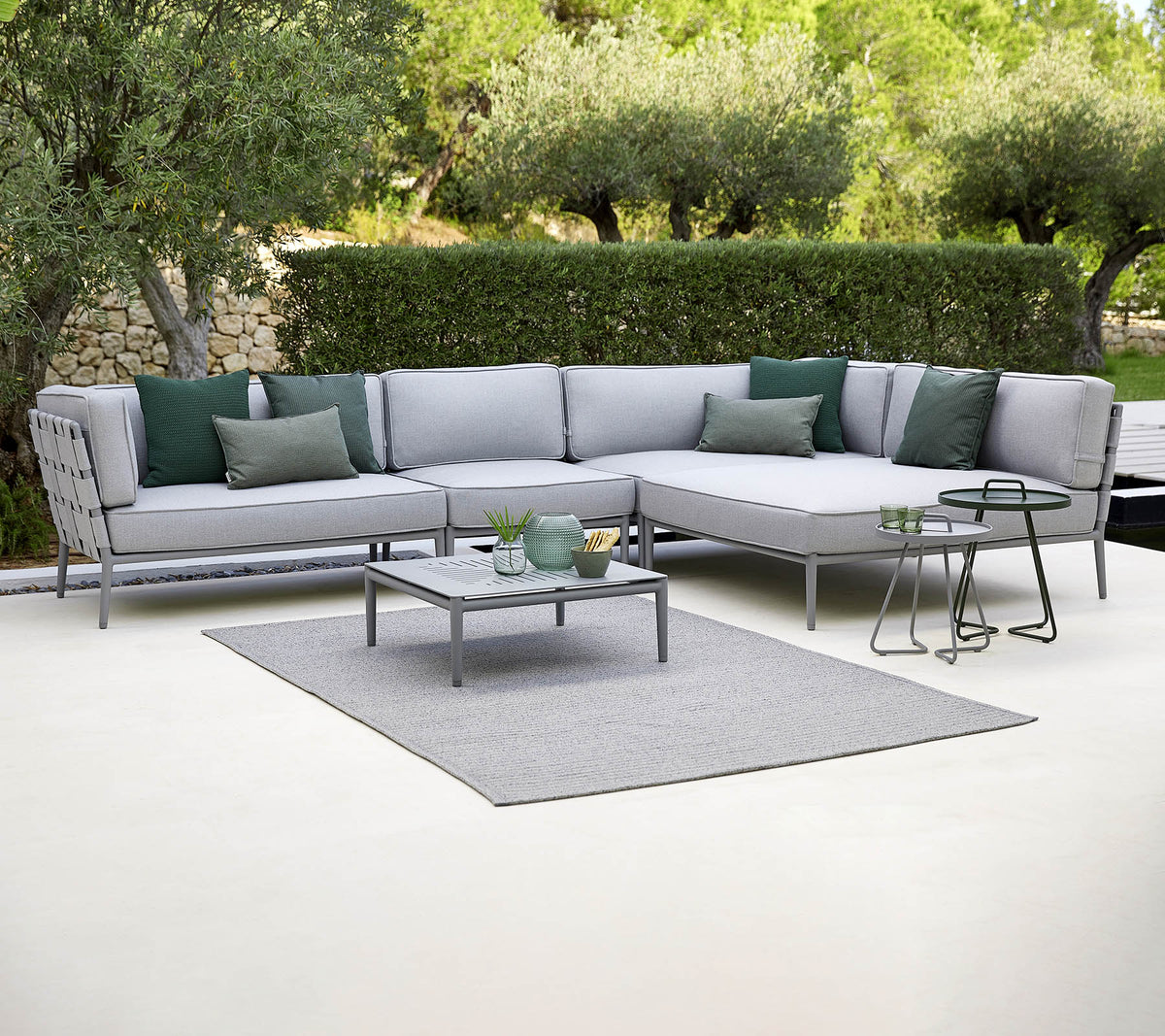 Stylische Garten-Landschaftssofa mit grünen Kissen, einem Couchtisch und einem Teppich, vor einem Hintergrund aus Grün.