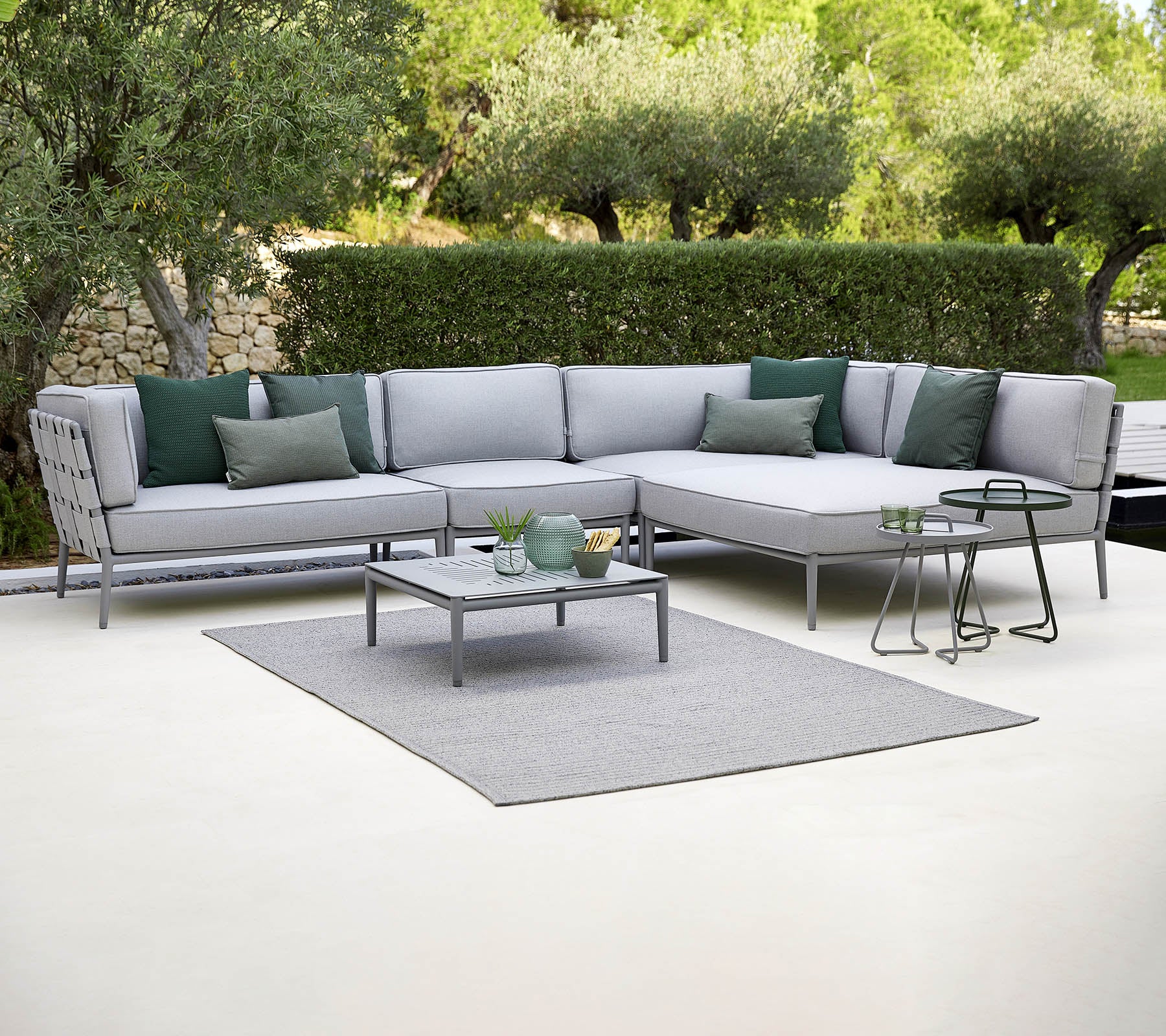 Stylische Garten-Landschaftssofa mit grünen Kissen, einem Couchtisch und einem Teppich, vor einem Hintergrund aus Grün.