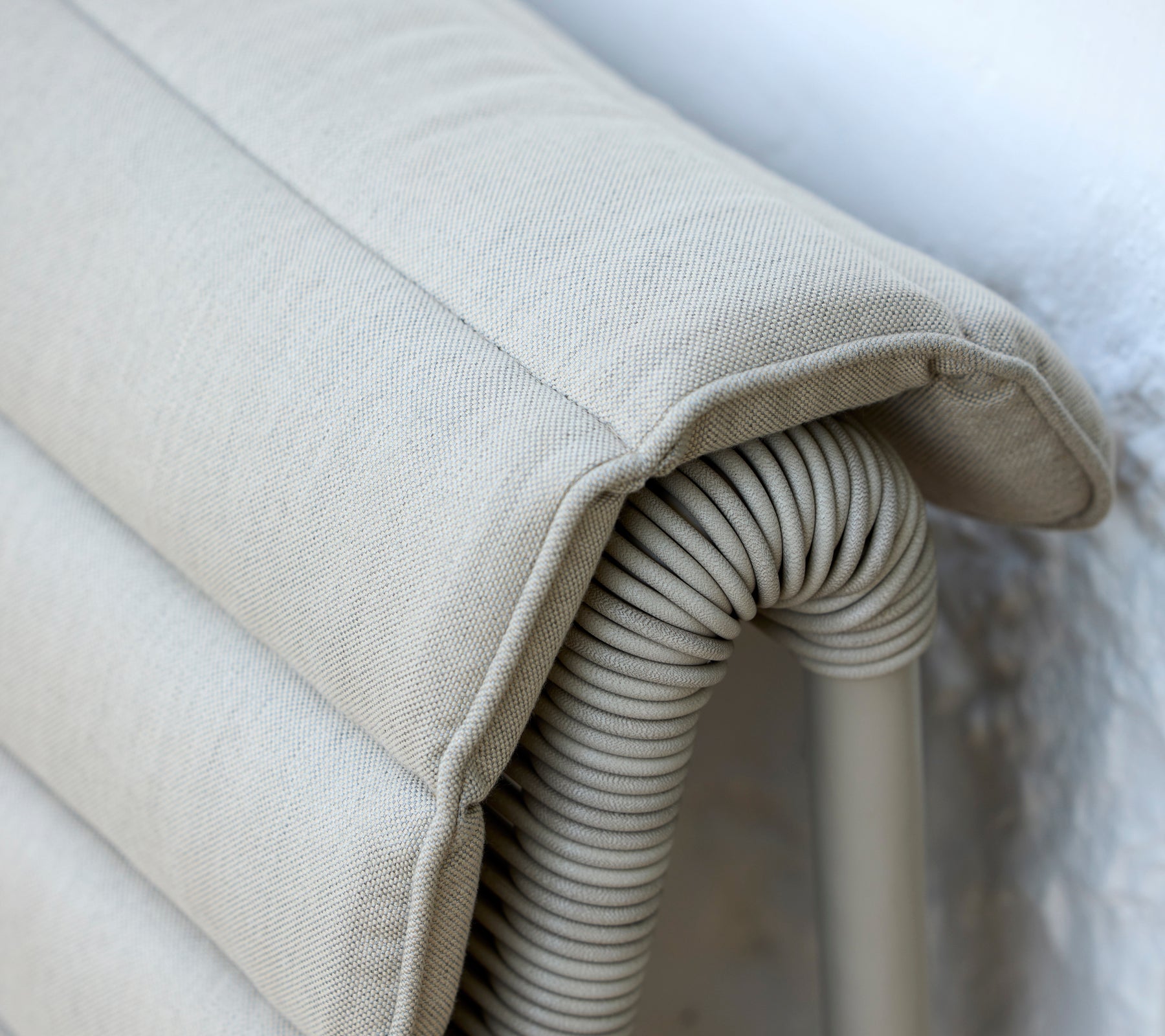 Beige Kissen mit gerippter Textur, das an einer hellen Wand lehnt.