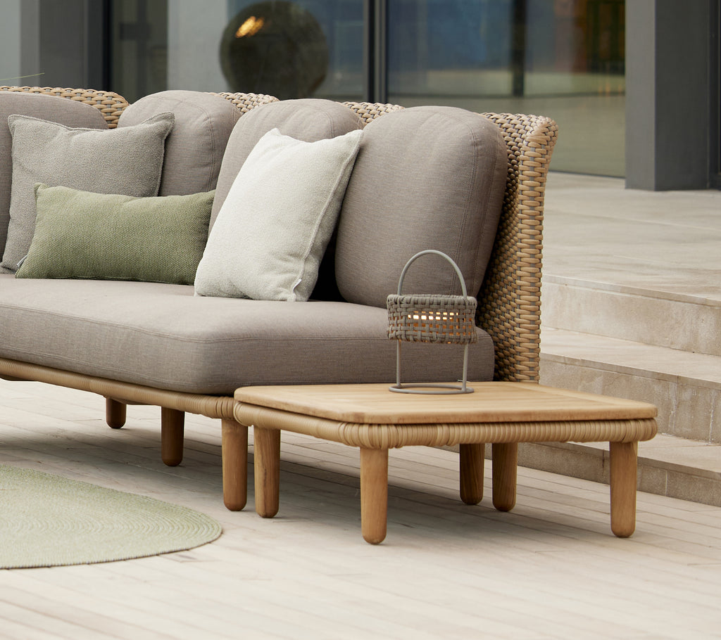 Stylischer Bogen-Kaffeetisch mit einer Teakholzoberfläche neben Kissen auf einem modernen Sofa, ergänzt durch eine dekorative Illusionlampe.