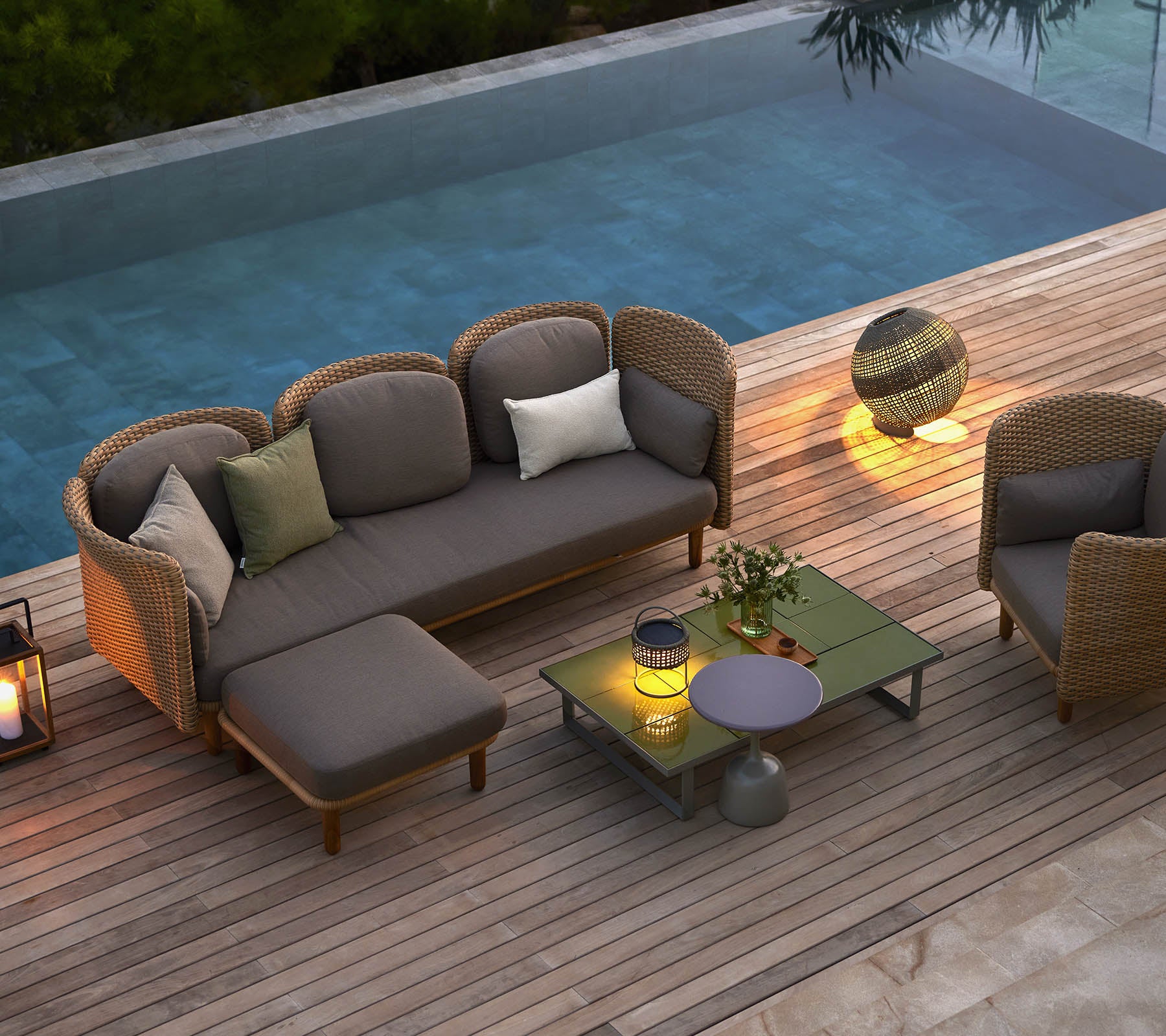 Stilvolle Loungemöbel mit Kissen, einem Couchtisch und ambienter Beleuchtung, neben einem ruhigen Pool.