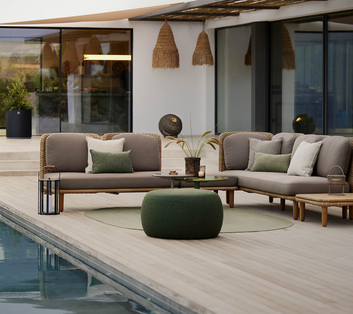 Ein stilvolles Lounge-Bereich mit einer Eckcouch mit Kissen, einem runden Tisch und einem gemütlichen Pouf, der neben einem ruhigen Pool steht.