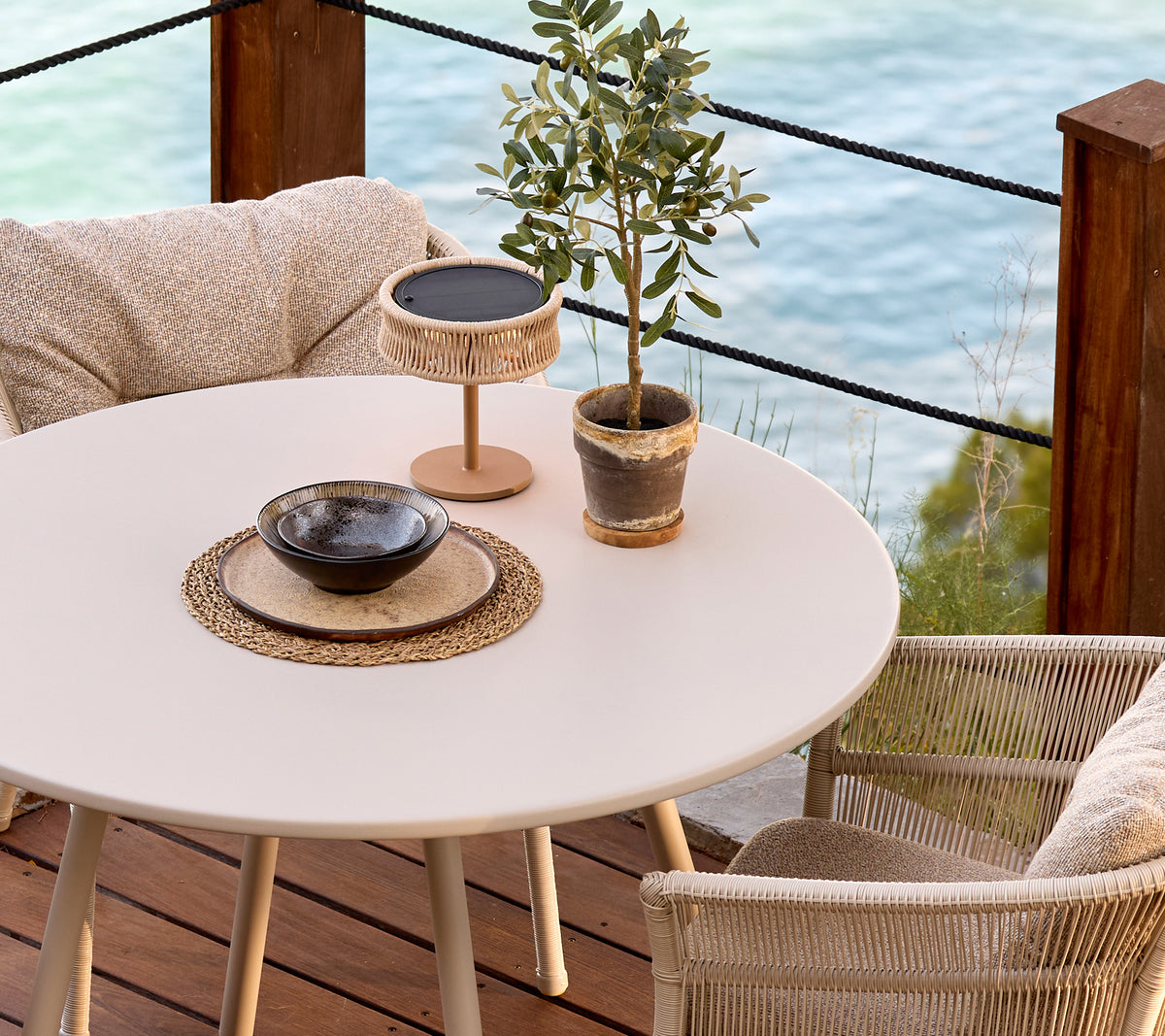 Weißer runder Tisch mit geflochtenen Stühlen, dekorativer Pflanze und einer schwarzen Schüssel in einem modernen Lounge-Setting.