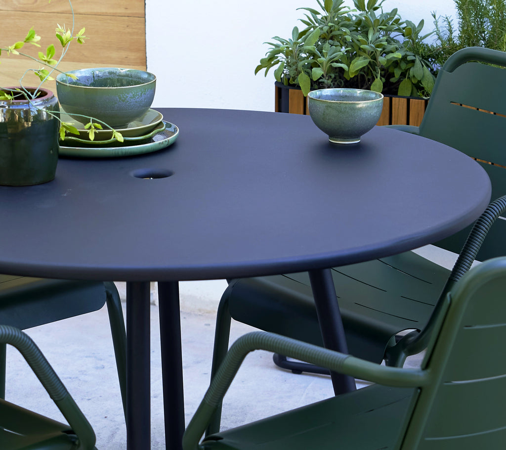 Runder grauer Tisch mit grünen Kopenhagener Stühlen, dekoriert mit Schalen und Pflanzen im Hintergrund.