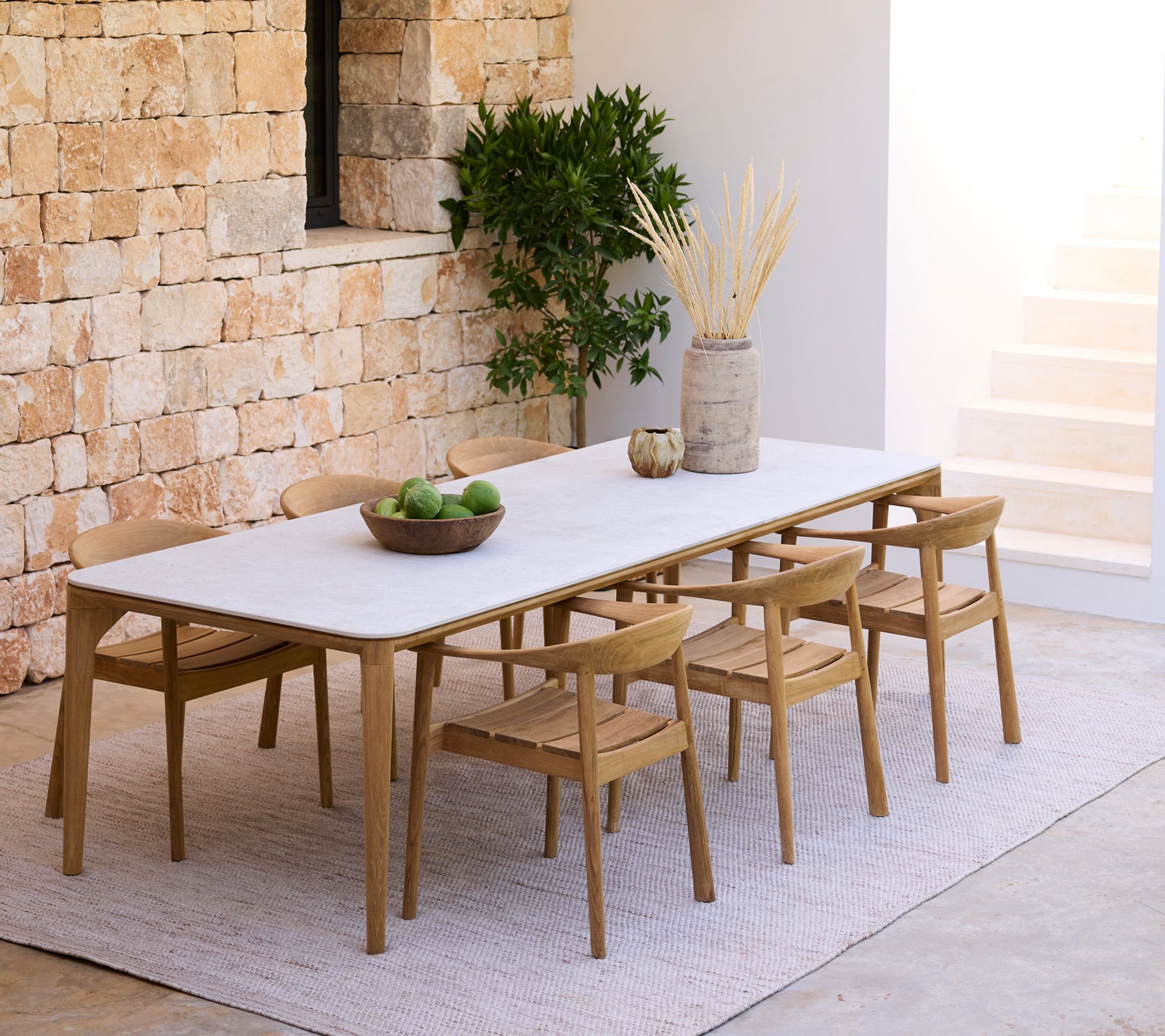 Moderne Essbereich mit einem weißen Tisch und Holzstühlen gegen eine Steinwand.