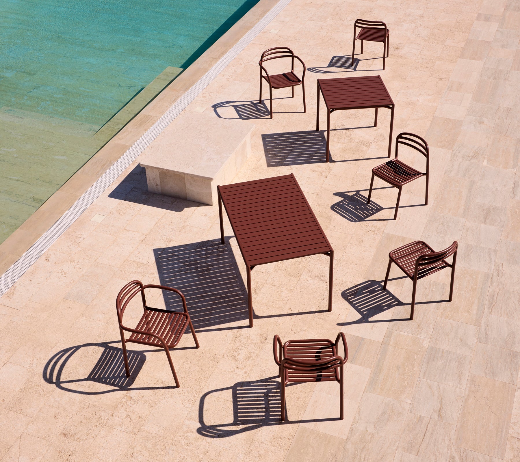 Bliss-Serie Gartenmöbel in Wüstenrot, angeordnet rund um einen Pool auf einer sonnigen Terrasse, die verspielte Schatten wirft.