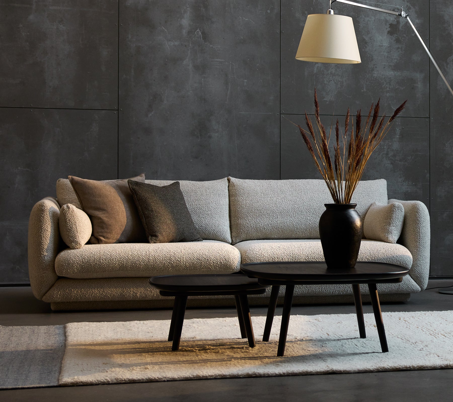 Bloom 3-Sitzer Sofa in Sandfarbe mit dekorativen Kissen, begleitet von zwei Pace-Couchtischen in verschiedenen Größen und einer stilvollen Stehlampe.