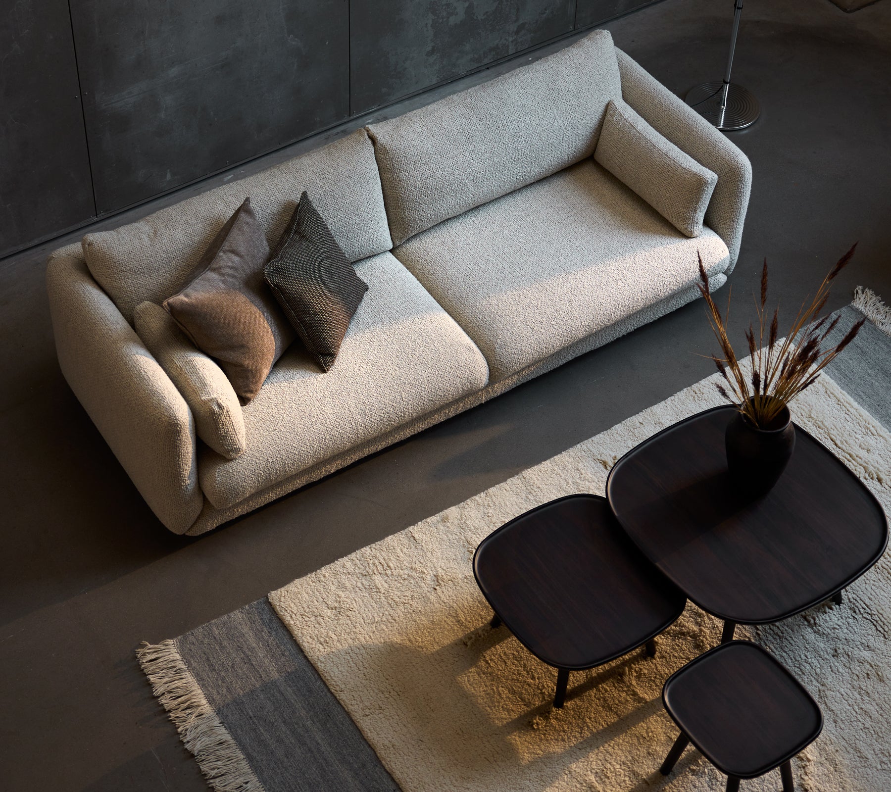 Stylische Dreisitzer-Sofa in Sandfarbe, ergänzt durch drei Größen von eleganten schwarzen Couchtischen und dekorativen Kissen.