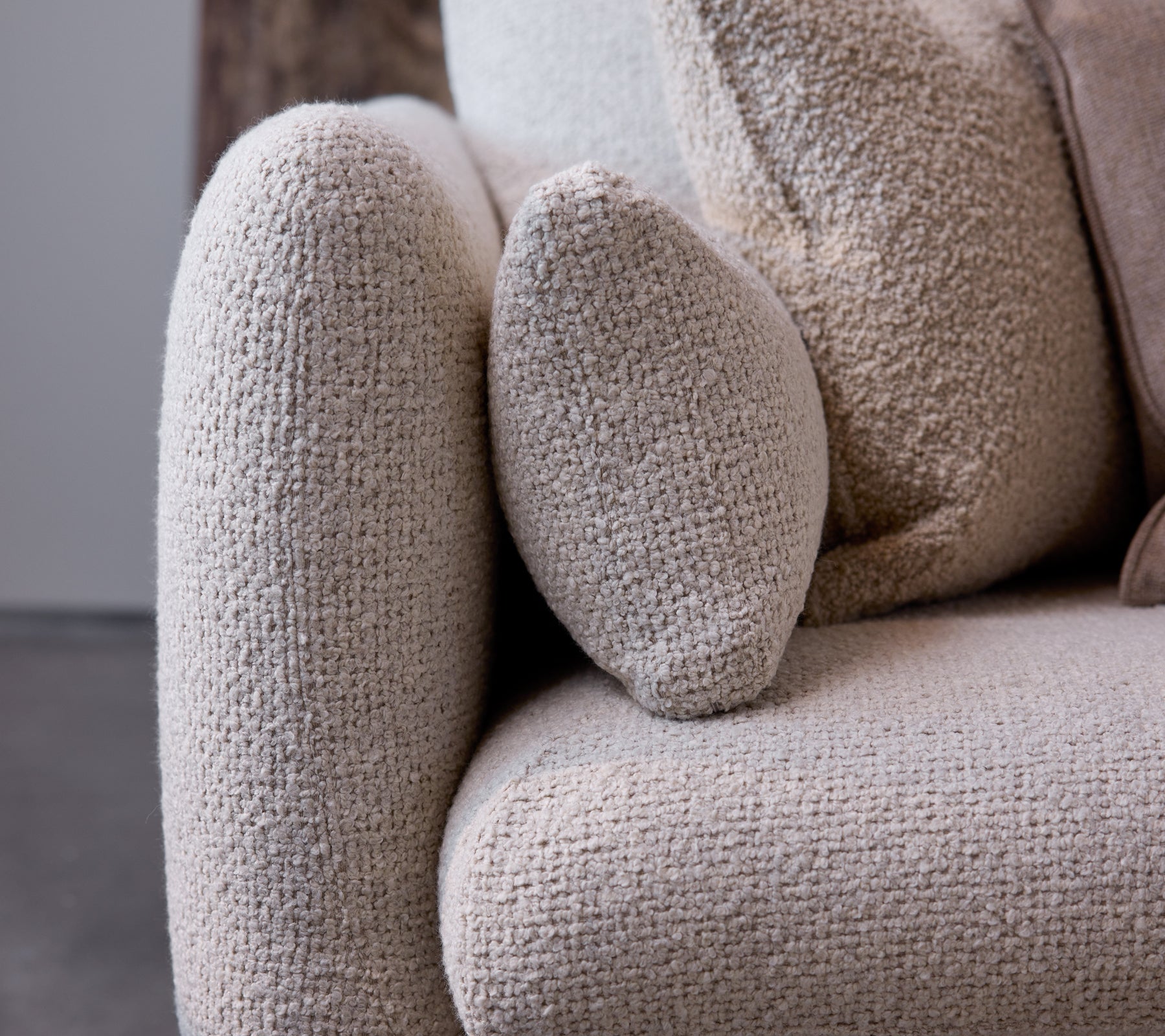 Nahaufnahme der Armlehne eines Bloom Sofas in einer Sand Flair Textur, die ein abgerundetes Design und einen weichen, gemütlichen Stoff zeigt.
