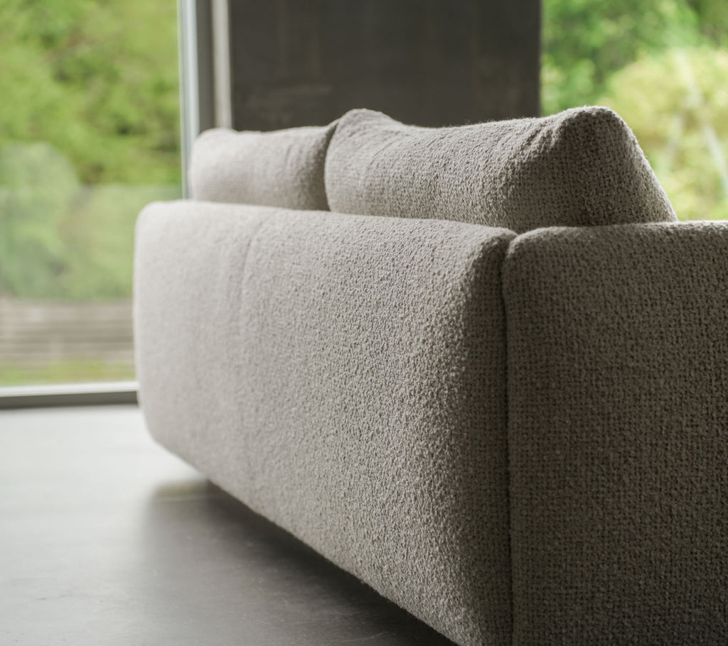 Zeitgenössisches Sofa mit einem strukturierten sandfarbenen Stoff, akzentuiert durch elegante Teakbeine, das Cane-line Flair und weiche Kissen zeigt.