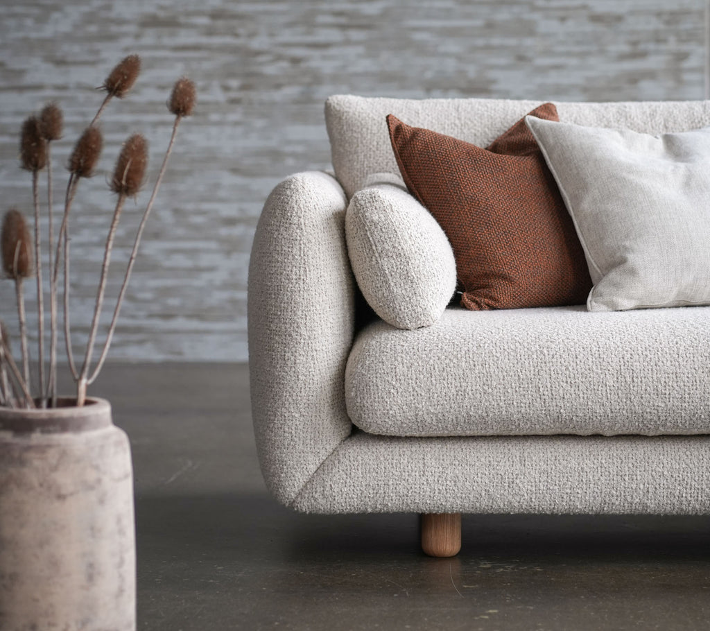 Gemütliches Sofa mit Blumendekor, Teakbeinen und erhöhten Kissen, begleitet von einer dekorativen Vase und getrockneten Blumen. Elegantes und einladendes Design.