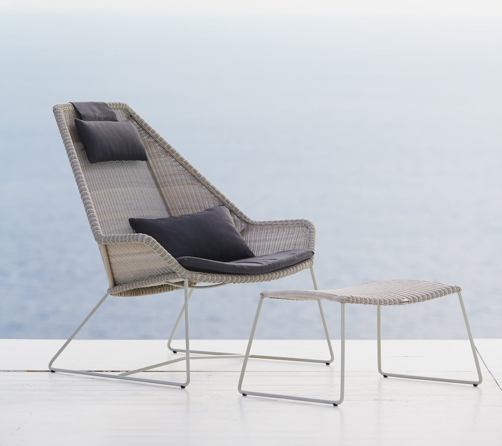 Moderne grauer Stuhl mit schwarzem Kissen und grauem Hocker vor einer malerischen Kulisse.