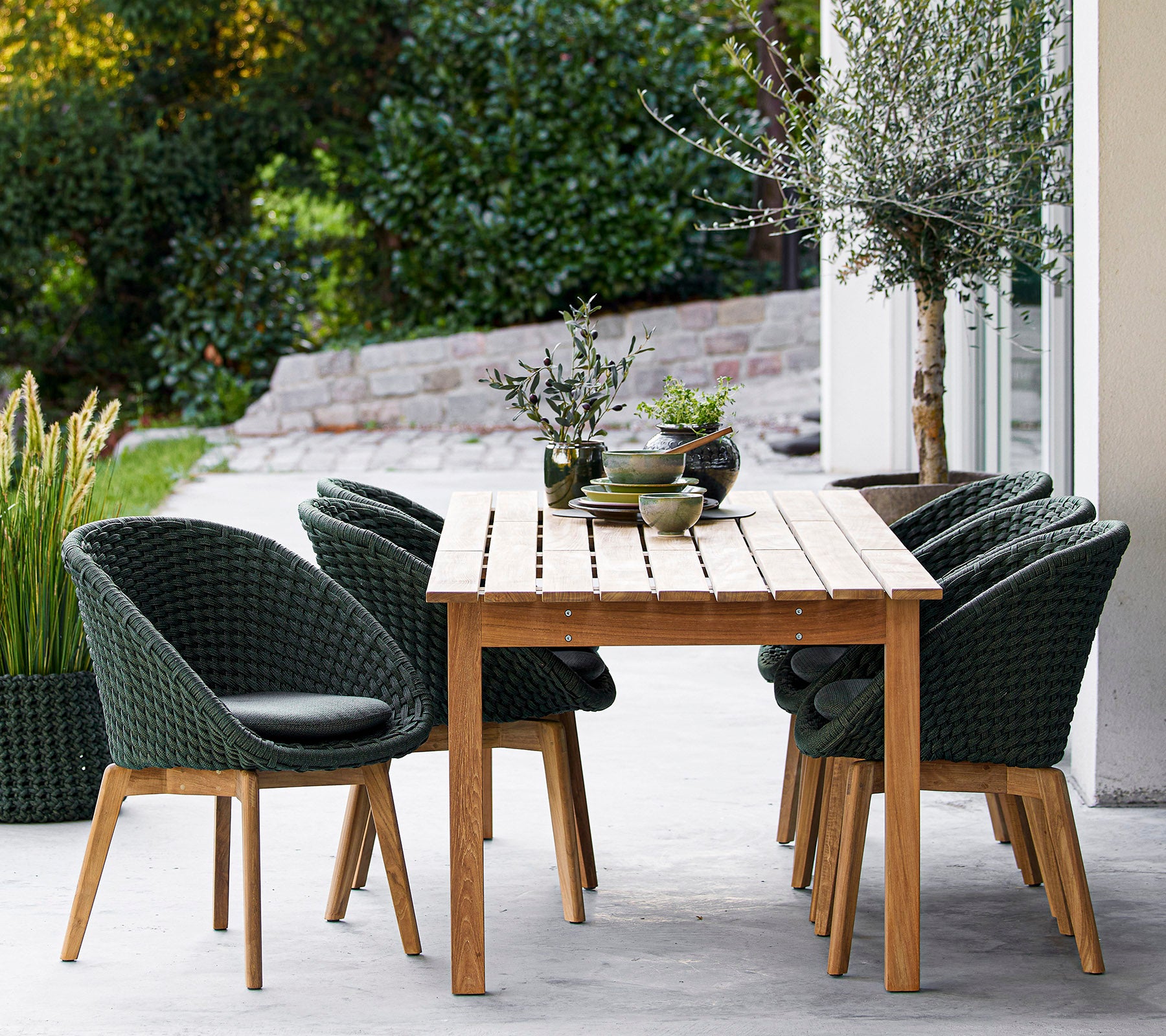 Ein Holztisch umgeben von stylischen grünen Stühlen, mit dekorativen Pflanzen und einem ruhigen Hintergrund. Ideal zum Essen oder Entspannen.