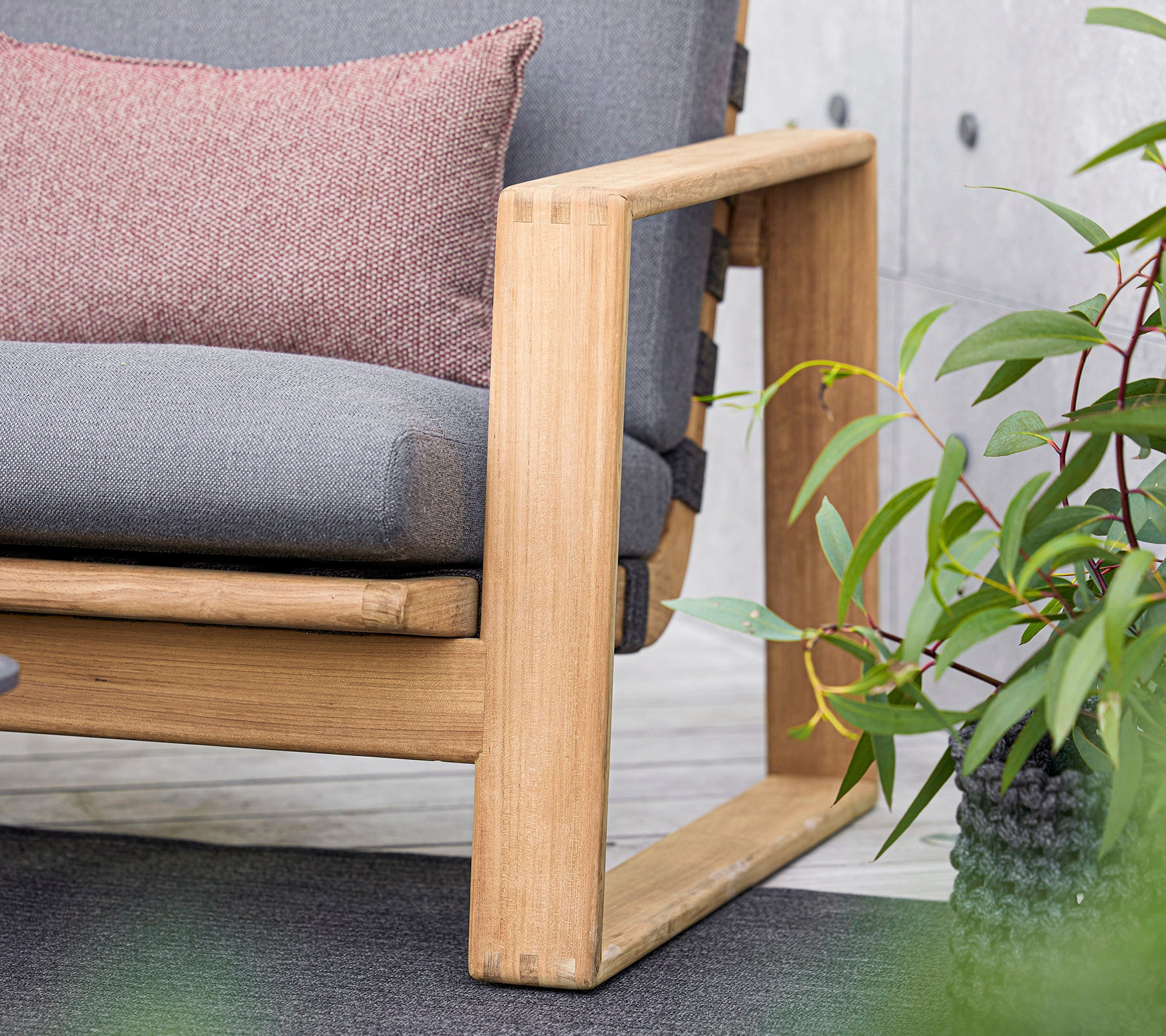 ein modernes Sofa mit einem Holzrahmen, das graue Kissen und ein dekoratives Kissen hat, ergänzt durch üppige grüne Pflanzen in der Nähe.