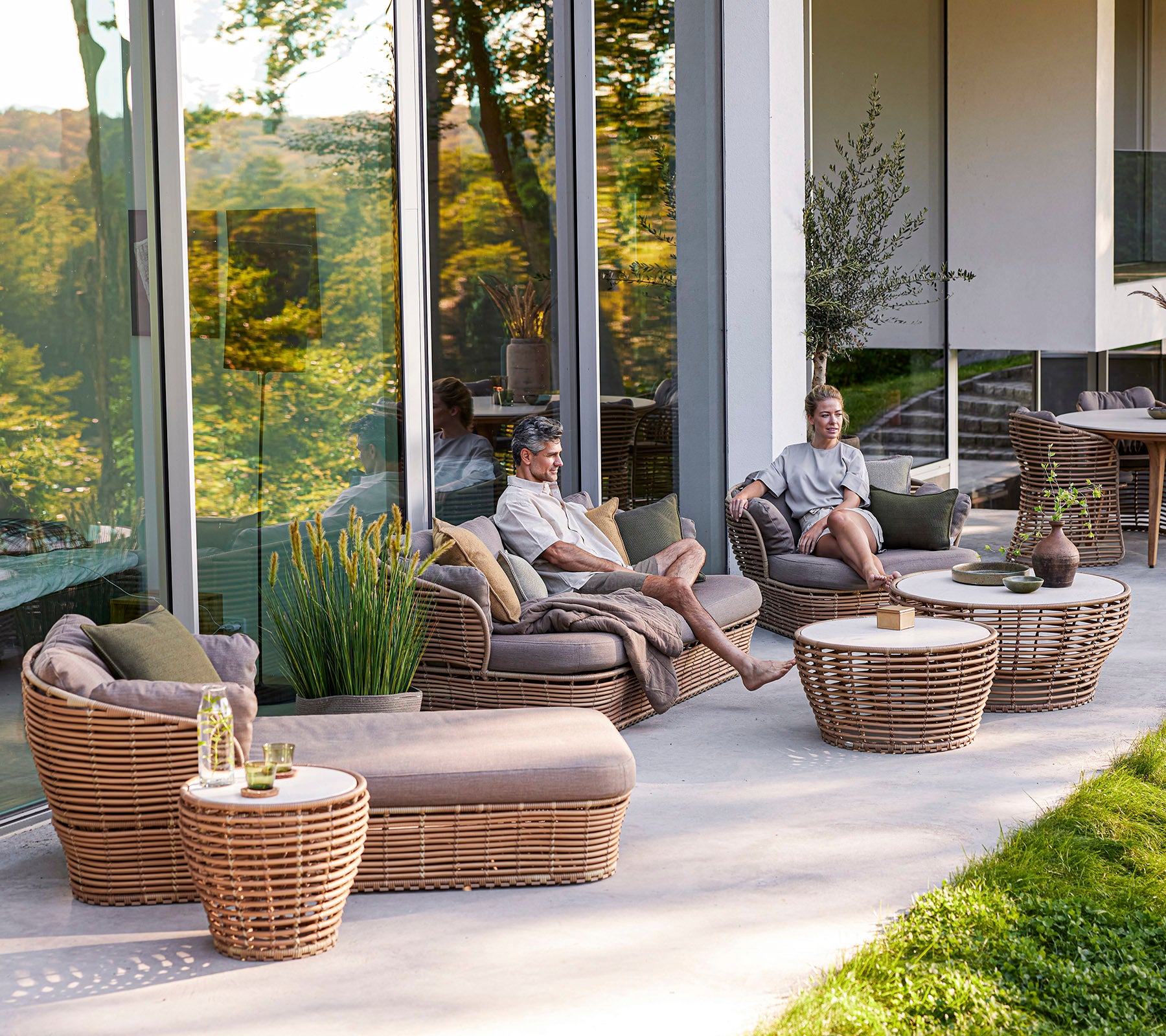 Ein entspannender Sitzbereich mit geflochtenen Möbeln, Kissen und niedrigen Tischen, wo zwei Personen ihre gemeinsame Zeit genießen.