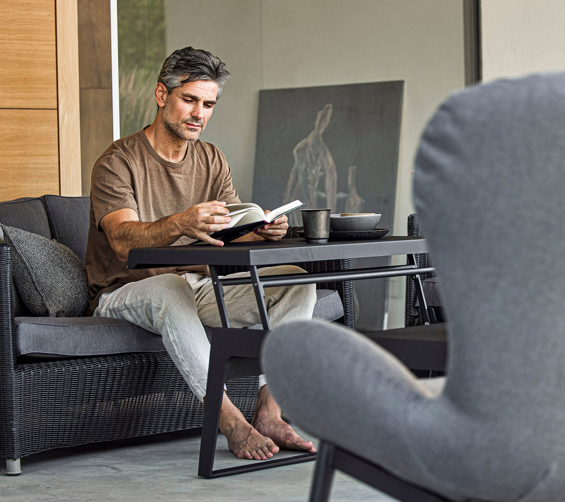 Ein Mann sitzt auf einem Sofa, liest ein Buch und hat eine Tasse neben sich in einer stilvollen und entspannten Umgebung.