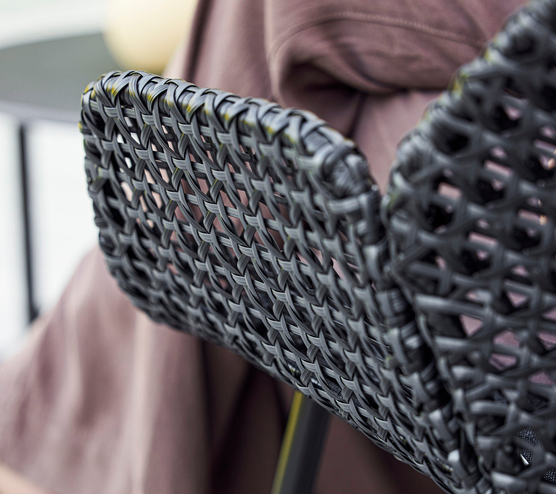 Schwarze gewebte Stuhlrücken mit einem strukturierten Design, ergänzt durch einen drapierten Stoff im Hintergrund.