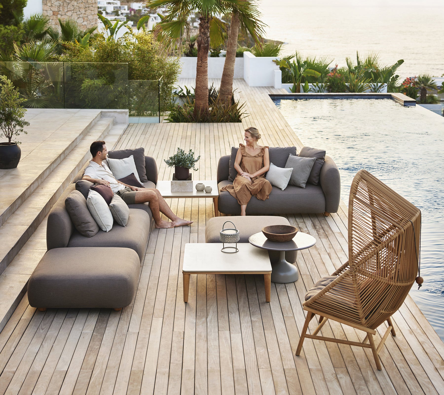 Moderne Außenlounge-Bereich mit grauen Sofas, einem weißen Tisch und einem Rattanstuhl.
