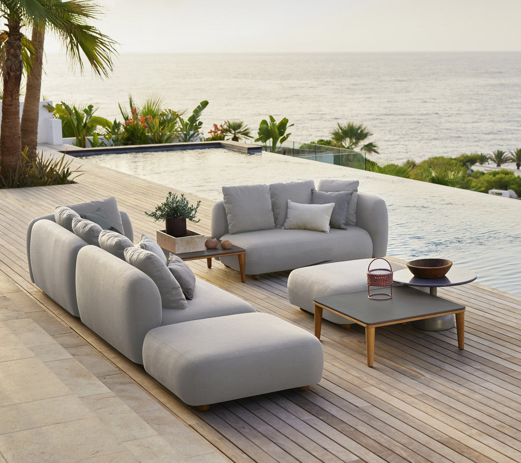 Stylische graue Sofa mit Kissen und einem schwarzen Couchtisch in einer modernen Außensitzgruppe am Meer.