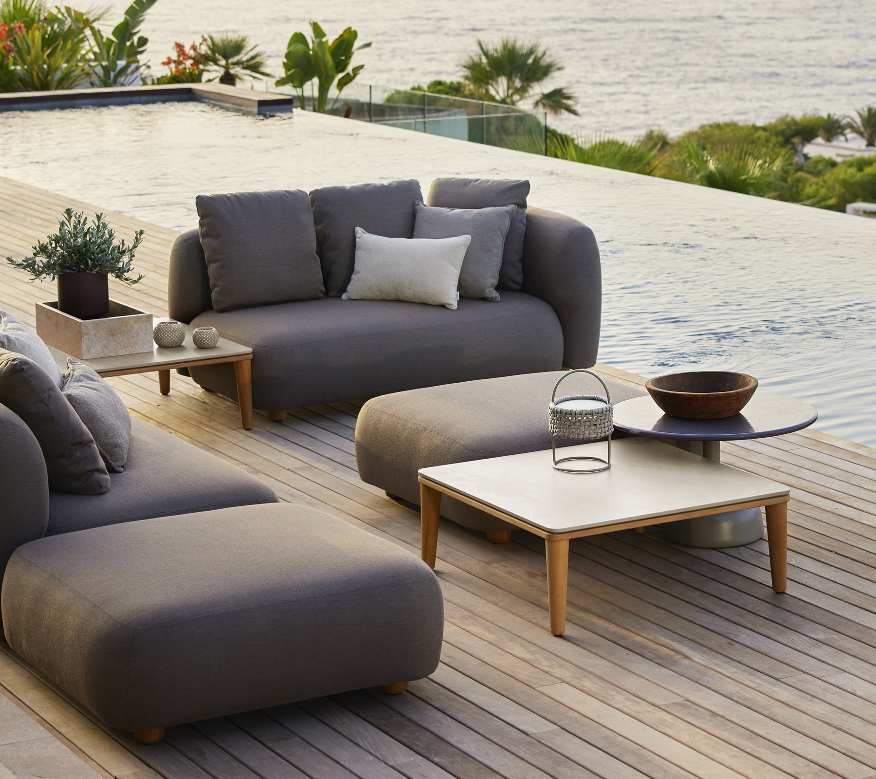 Moderne Loungemöbel für den Außenbereich mit grauem Sofa, Stuhl und Holztisch.