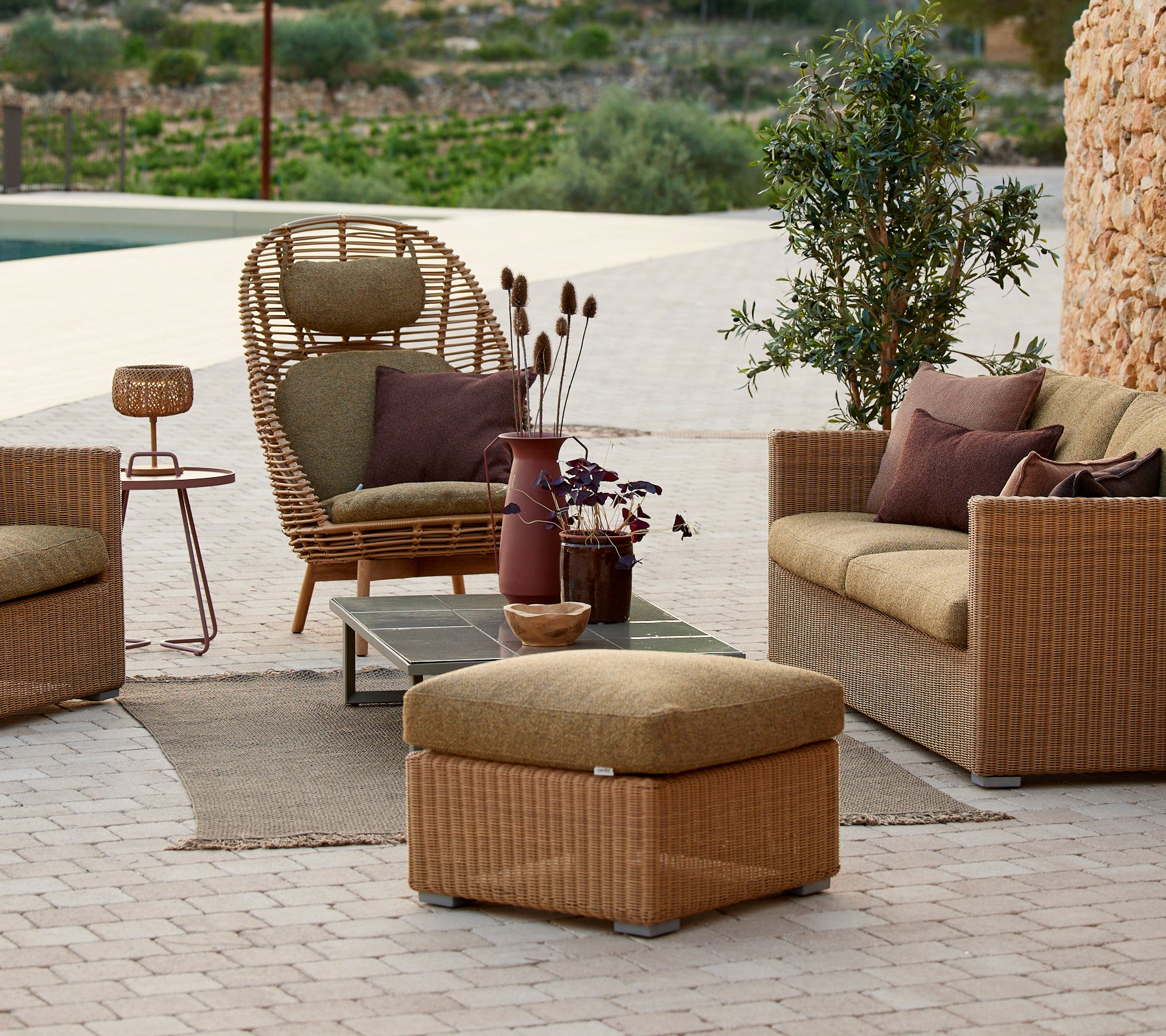 Lounge-Sitzbereich mit Rattanstuhl, beigem Sofa und Beistelltisch mit einer lila Vase.