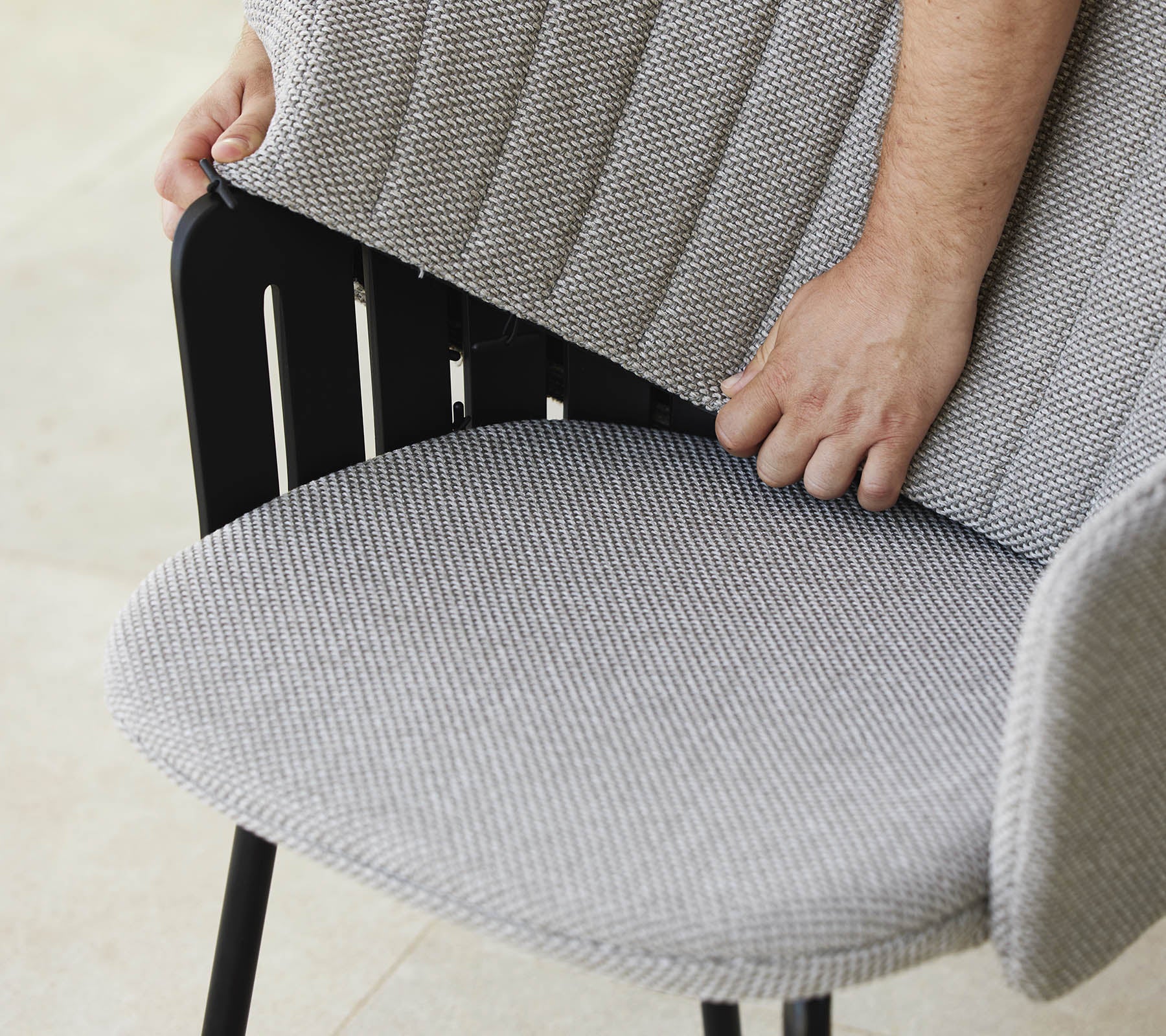 Person passt die Rückenlehne eines modernen Stuhls mit einem strukturierten Stoffsitz an, der ein stilvolles Design und ergonomische Unterstützung zeigt.