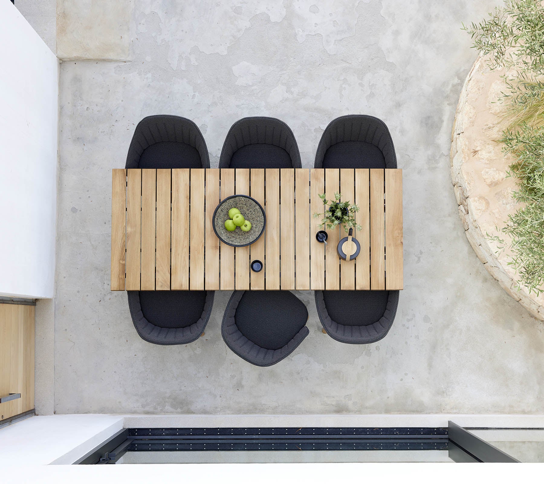 Stilvolles Holztisch mit vier schwarzen Stühlen, versehen mit einer Schüssel grüner Früchte und dekorativen Pflanzen für einen modernen Akzent.