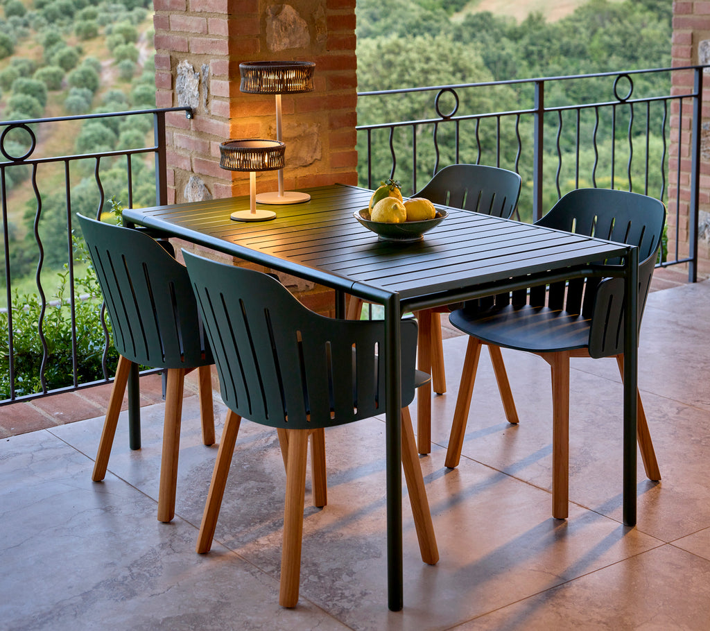 Ein stilvolles Esszimmer-Setup mit einem grünen rechteckigen Tisch, umgeben von schwarzen Essstühlen, ergänzt durch ein Obstzentrum und eine Lampe.