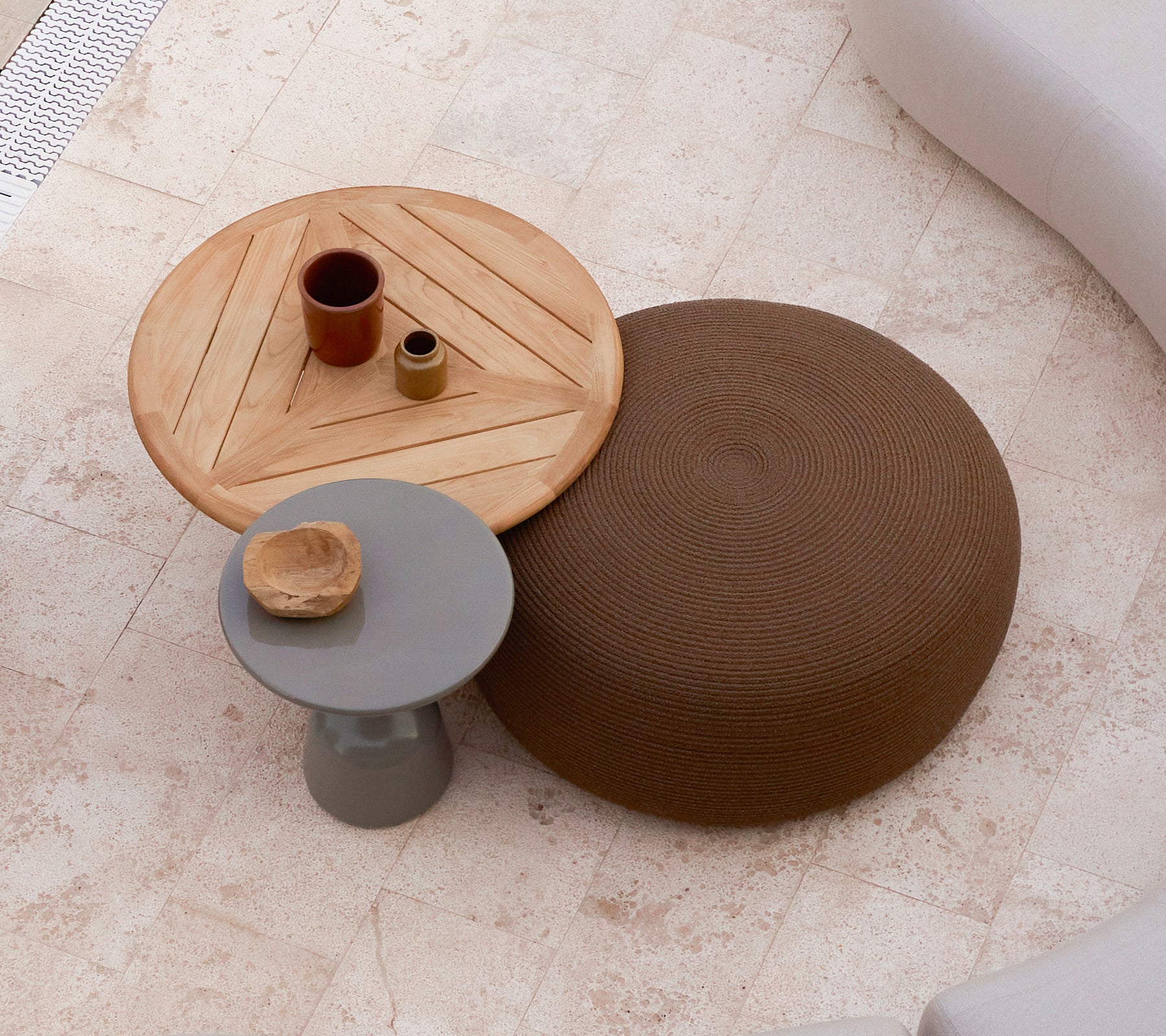 Ein großer runder Fußhocker in Braun neben einem Holztisch mit geometrischem Design, der kleine Dekorationsgegenstände oben hat.