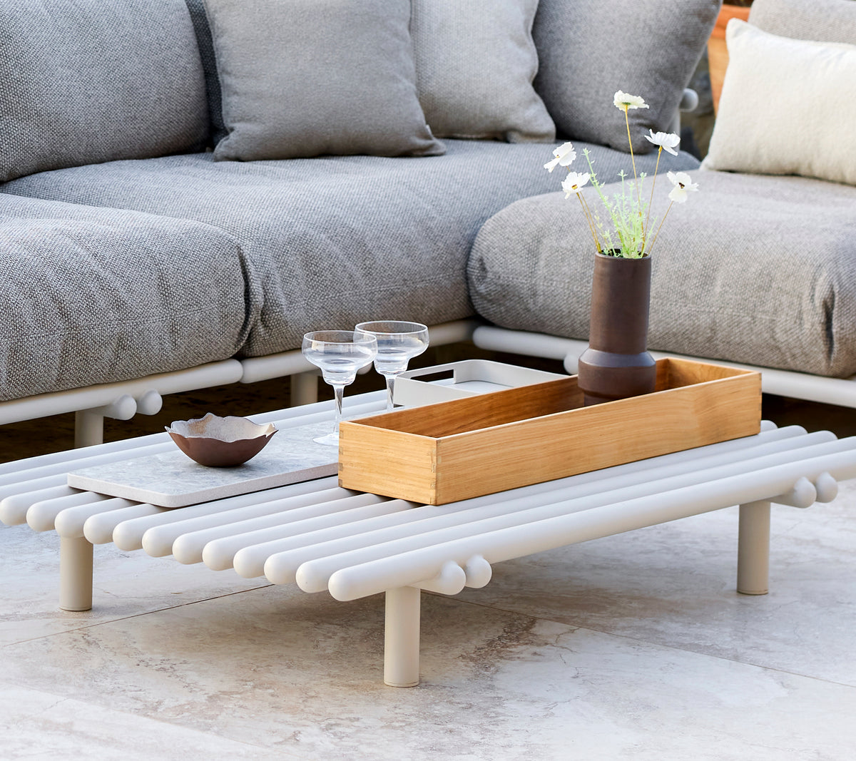 Ein stilvoller Couchtisch mit einer Teakholz-Aufbewahrungsbox, der ein minimalistisches Design und dekorative Elemente wie Gläser und eine kleine Vase aufweist.