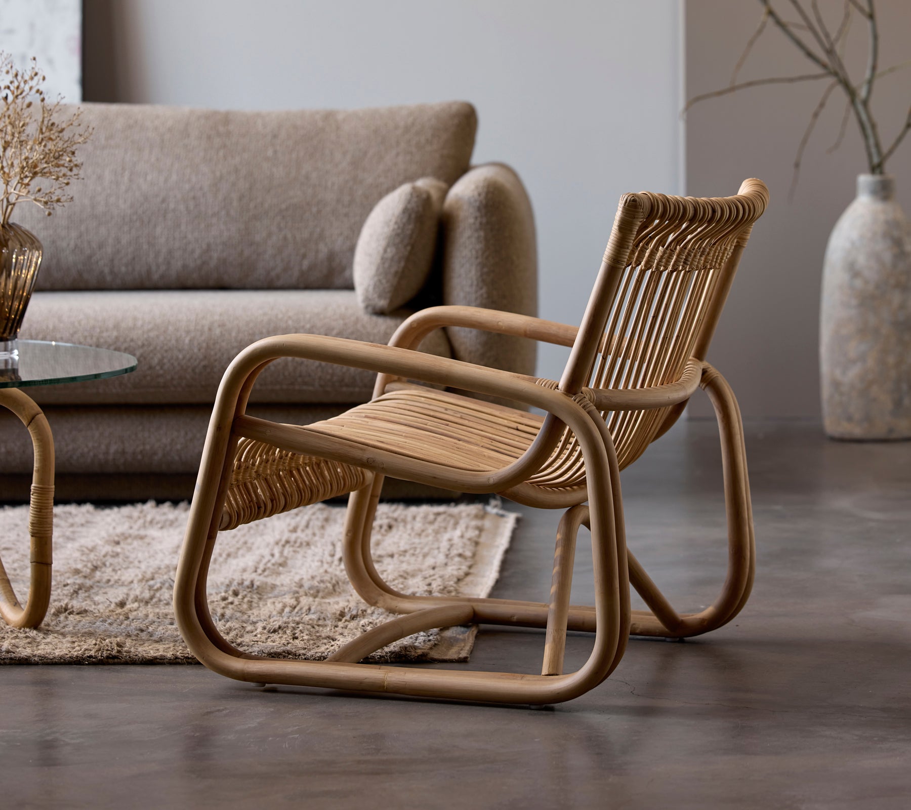 Rattanstuhl neben einem beigen Sofa und einem Glastisch in einem modernen Lounge-Setting.