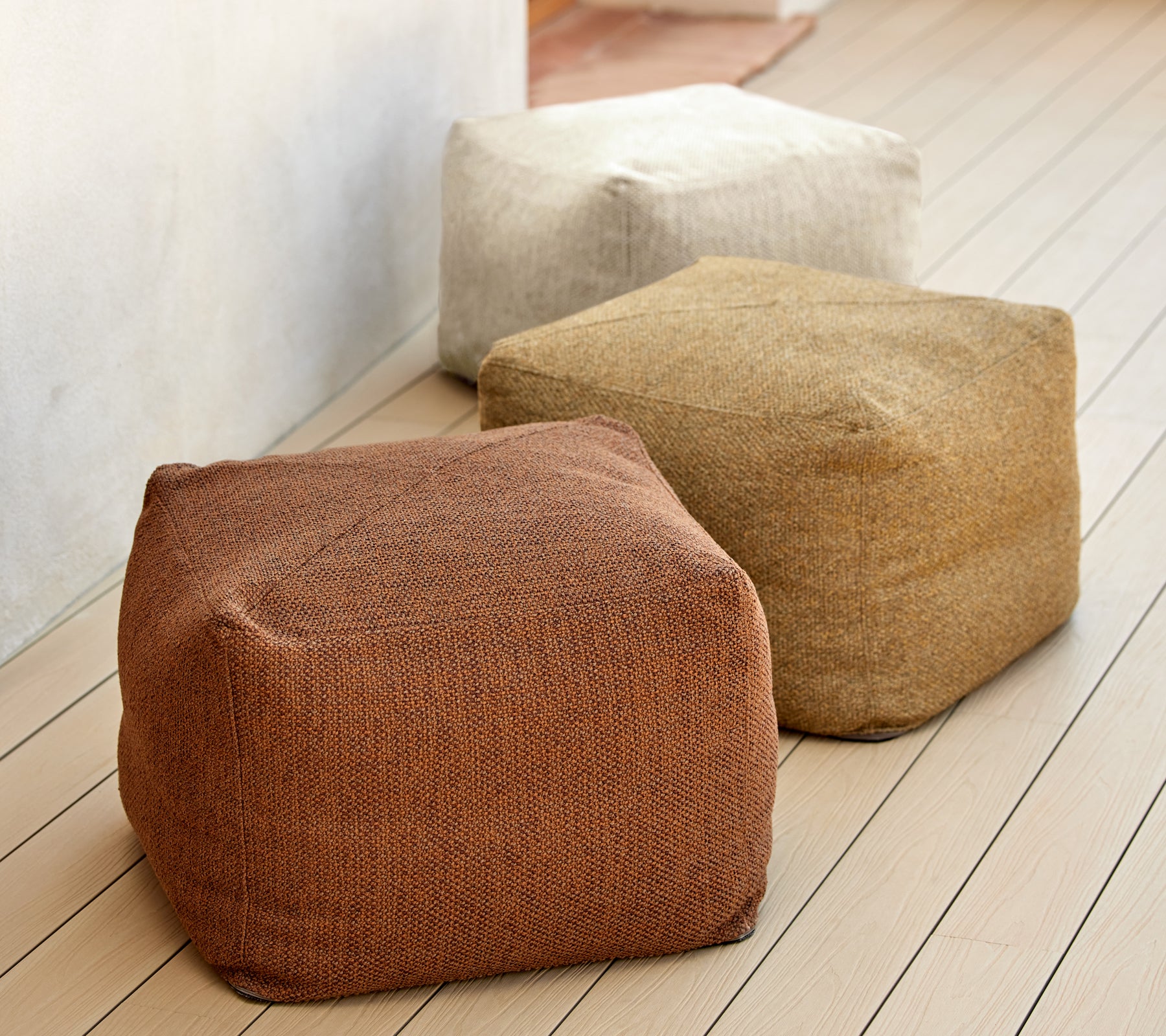 Drei strukturierte Poufs in erdigen Tönen von Braun, Beige und Tan, auf einer Holzoberfläche präsentiert. Ideal für vielseitige Sitzgelegenheiten und Dekoration.