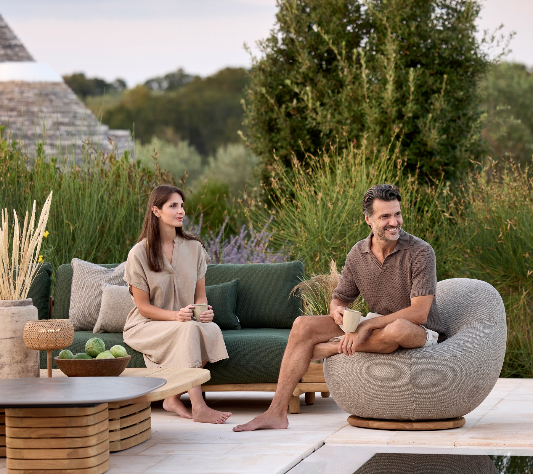 Moderne Lounge mit grünem Sofa, grauem Rundstuhl und braunem Tisch, umgeben von Grünpflanzen.
