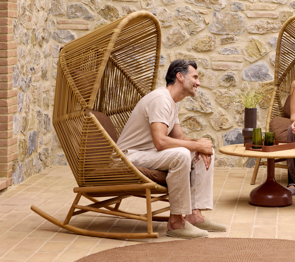 Ein stilvoller Hive Schaukelstuhl mit einem Rise Kissen-Set, in dem ein Mann einen entspannten Moment genießt. Modernes Design mit natürlichen Elementen.