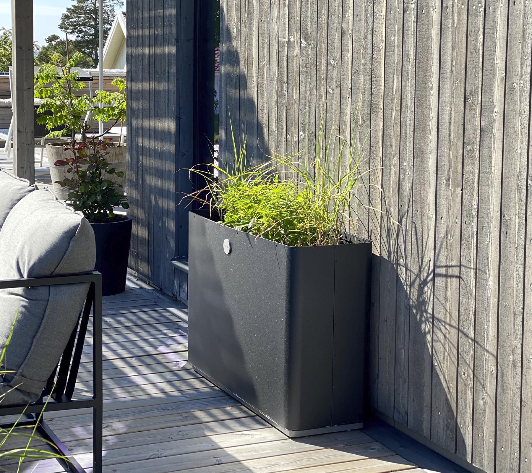 Ein schlanker, moderner Pflanztopf mit lebendigem Grün steht gegen eine strukturierte Holzwand und ergänzt den umliegenden Raum.