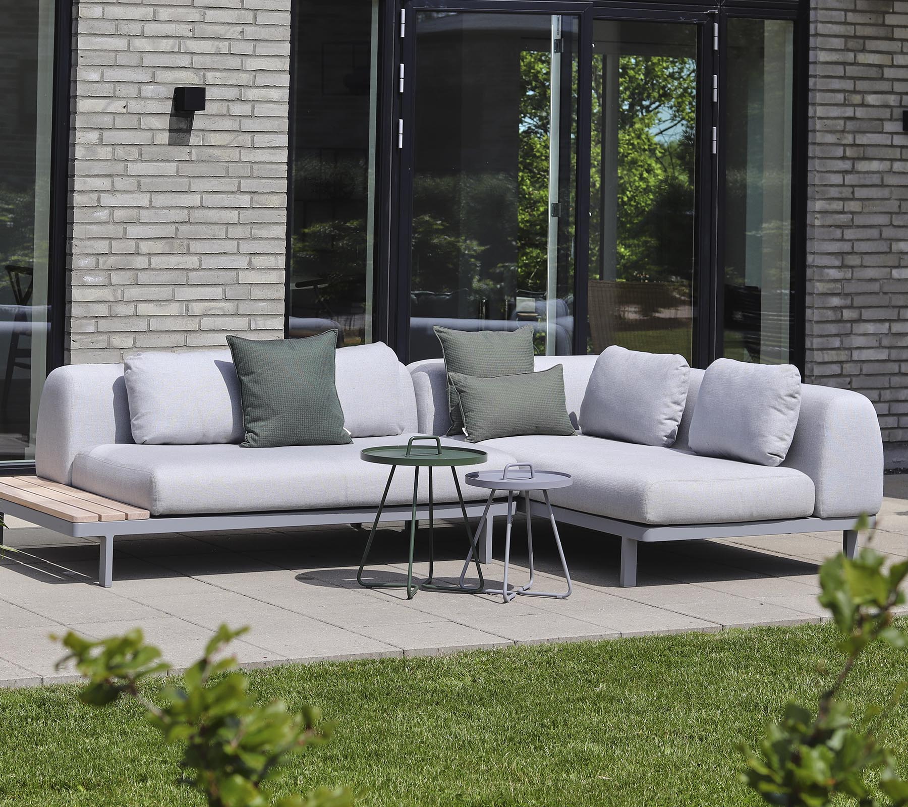Modernes Ecksofa aus hellem Stoff mit dekorativen Kissen, kombiniert mit kleinen Beistelltischen in einer ruhigen Umgebung.