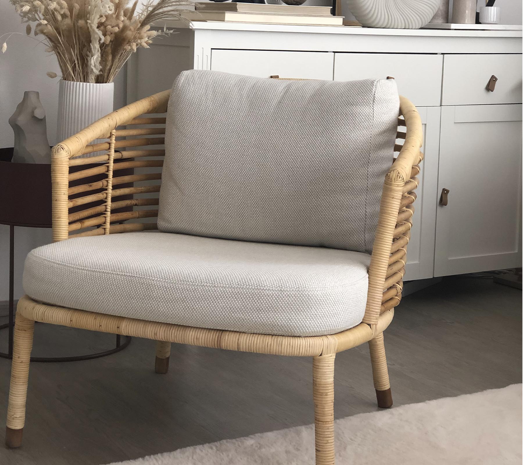 Ein stilvoller Stuhl mit einem gewebten Design und weichen Kissen, kombiniert mit einer dekorativen Pflanze und einem stilvollen Aufbewahrungseinheit im Hintergrund.