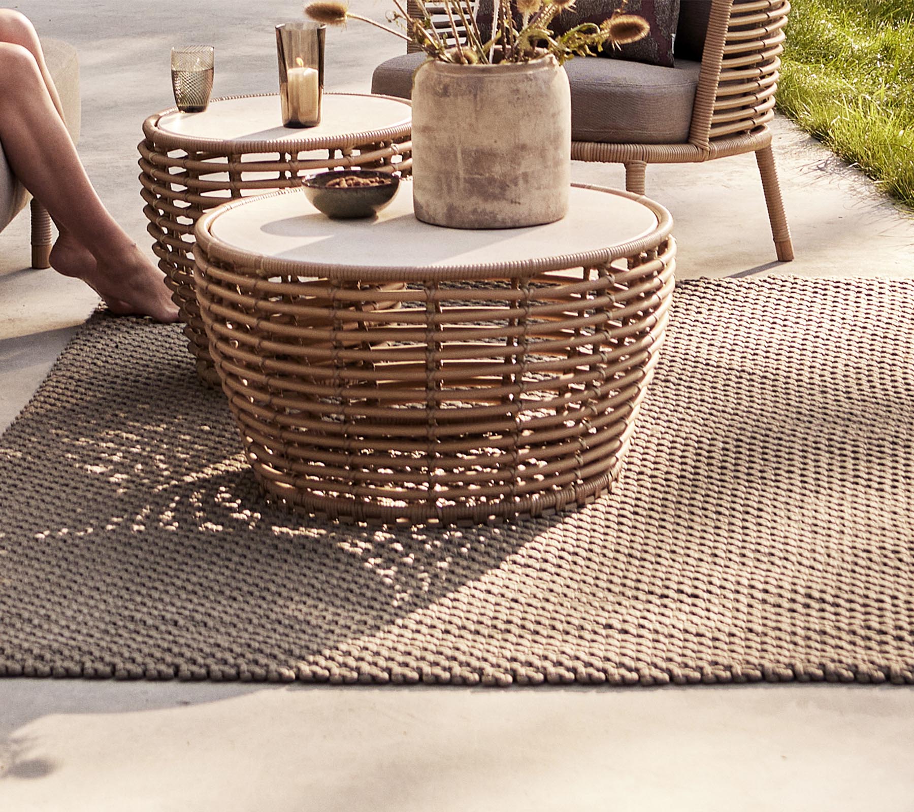 Ein gemütlicher Sitzbereich mit geflochtenen Tischen, einer dekorativen Vase und einem strukturierten Teppich, perfekt um einen stilvollen Raum zu bereichern.