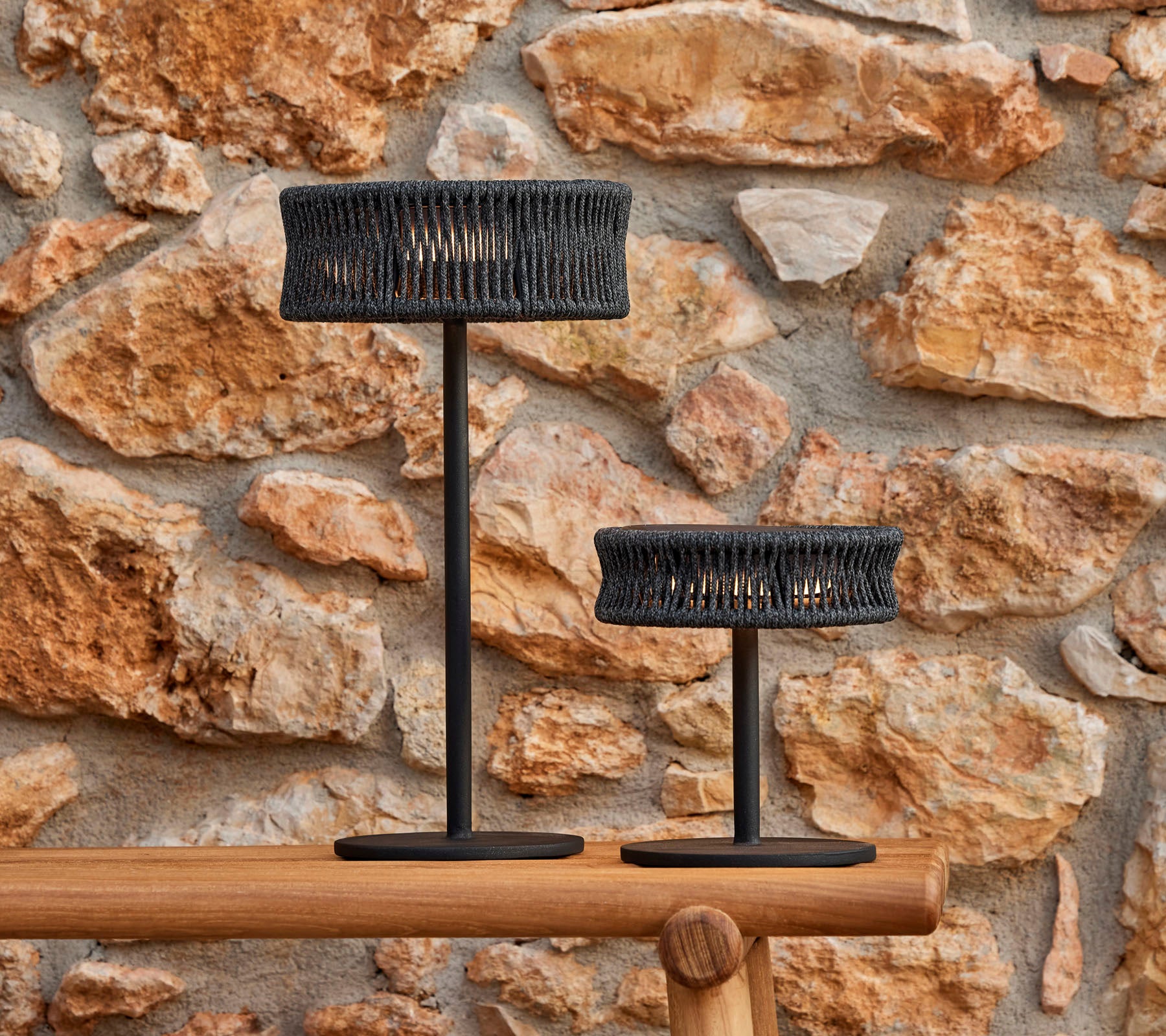 Zwei stilvolle Tischlampen mit einem gewebten Design, vor einer strukturierten Steinwand, die eine elegante und einladende Atmosphäre schafft.