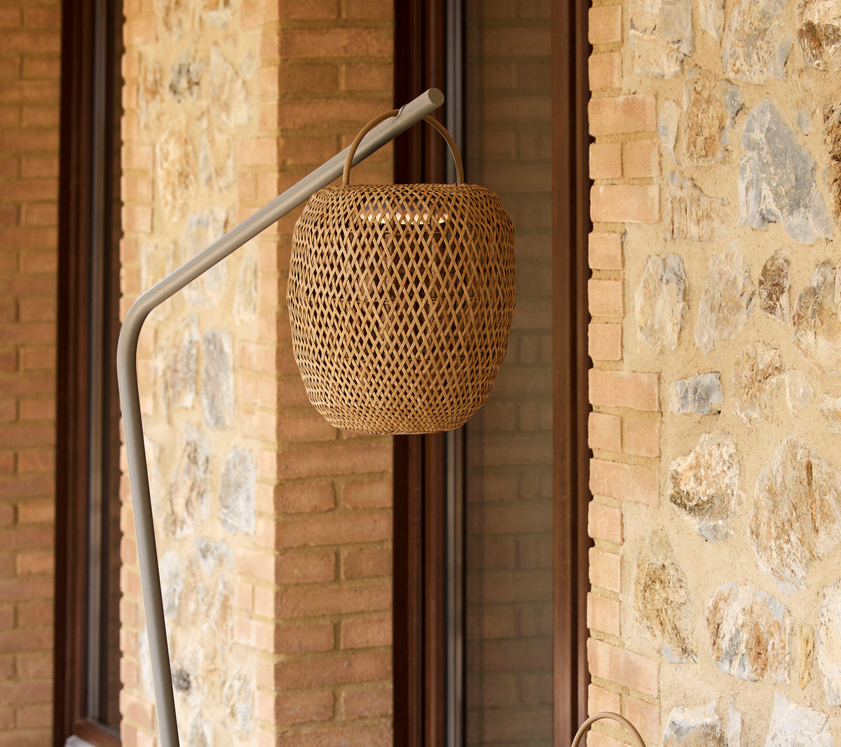 Eine gewebte leuchtende Lampe, die an einem schlanken Ständer hängt und eine strukturierte Steinwand ergänzt.