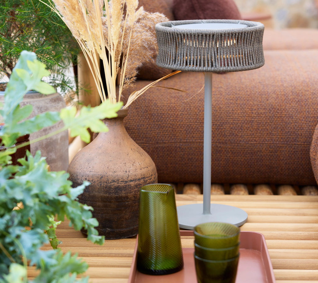 Eine mittelgroße Illusionslampe auf einem Clubtablett, umgeben von grünen Gläsern und dekorativen Pflanzen.