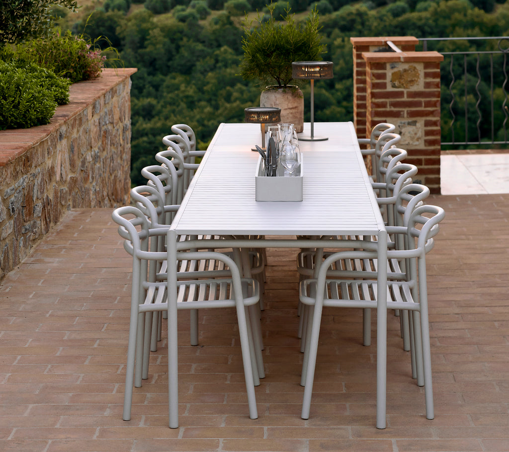 Ein langer, weißer Tisch, umgeben von mehreren eleganten, hellen Stühlen, mit dekorativen Gegenständen und Grünpflanzen, die das stilvolle Ambiente unterstreichen.