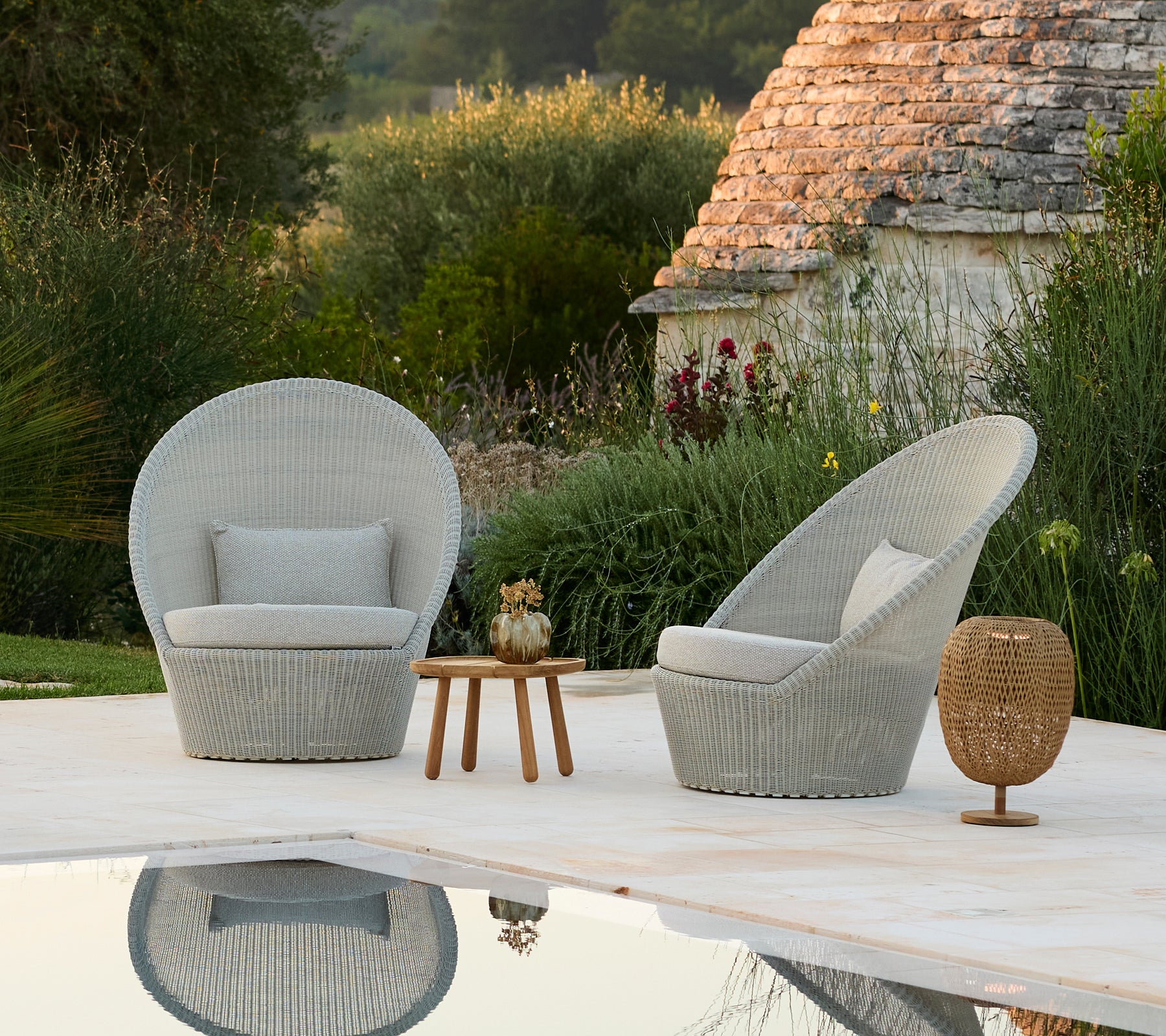 Zwei graue Lounge-Stühle und ein Holztisch neben einem Pool in einer modernen Außeneinstellung.