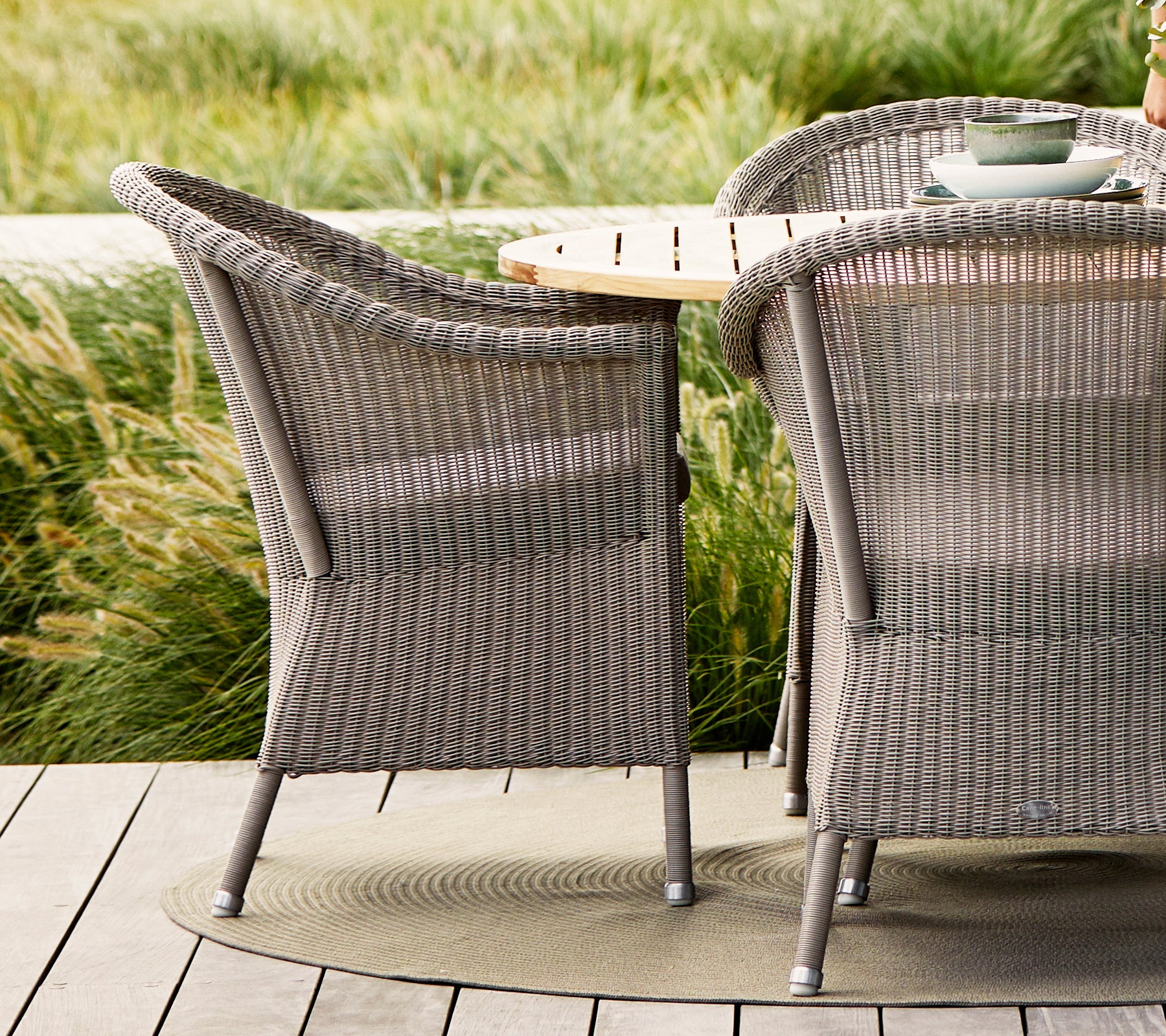 Taupe Lansing-Stühle mit strukturiertem Gewebe-Design, kombiniert mit einem Tisch aus Naturholz und umgeben von üppigem Grün.