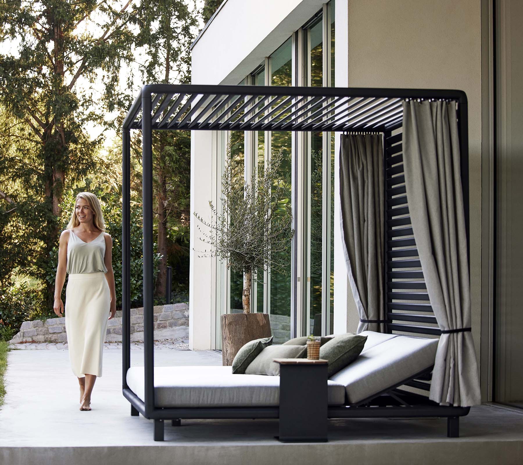 Eine stilvolle Cabana mit einem eleganten Design, weichen Kissen, Vorhängen und einem kleinen Beistelltisch, eingebettet in eine ruhige, natürliche Umgebung.