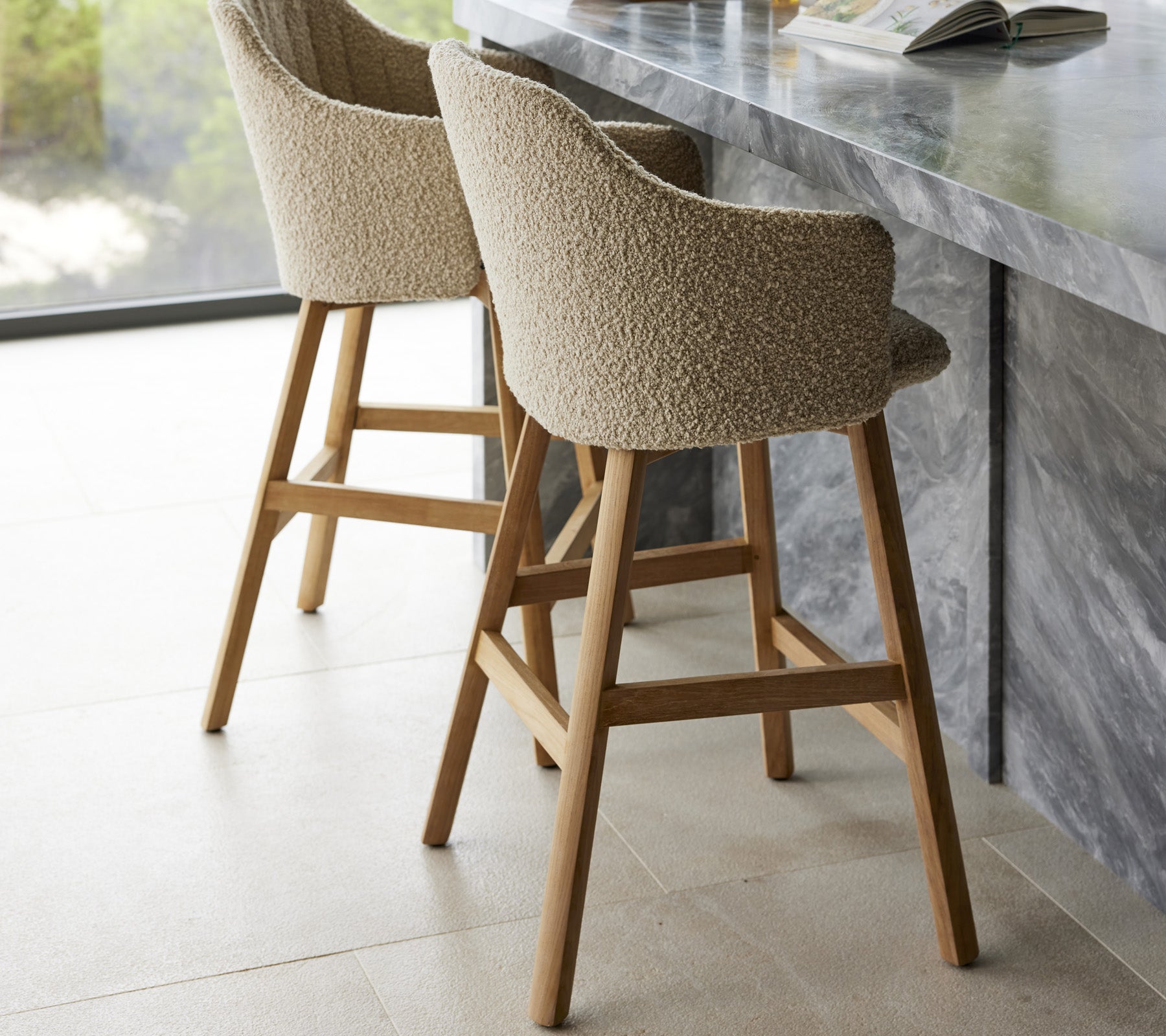Zwei moderne Barhocker mit gepolsterten Sitzen und Holzbeinen, die in der Nähe einer eleganten Marmor-Theke stehen.