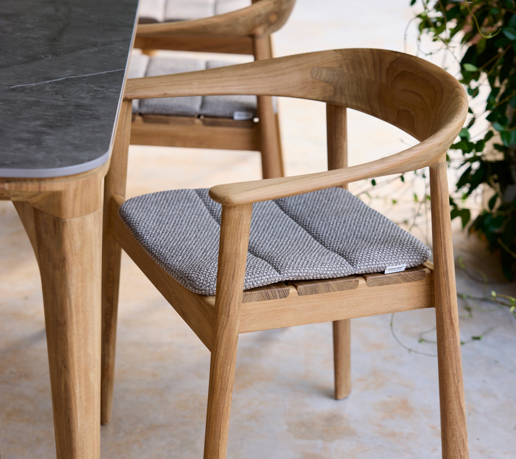 Moderne Holzstuhl mit grauem Kissen neben einem Tisch in einer Lounge-Umgebung.