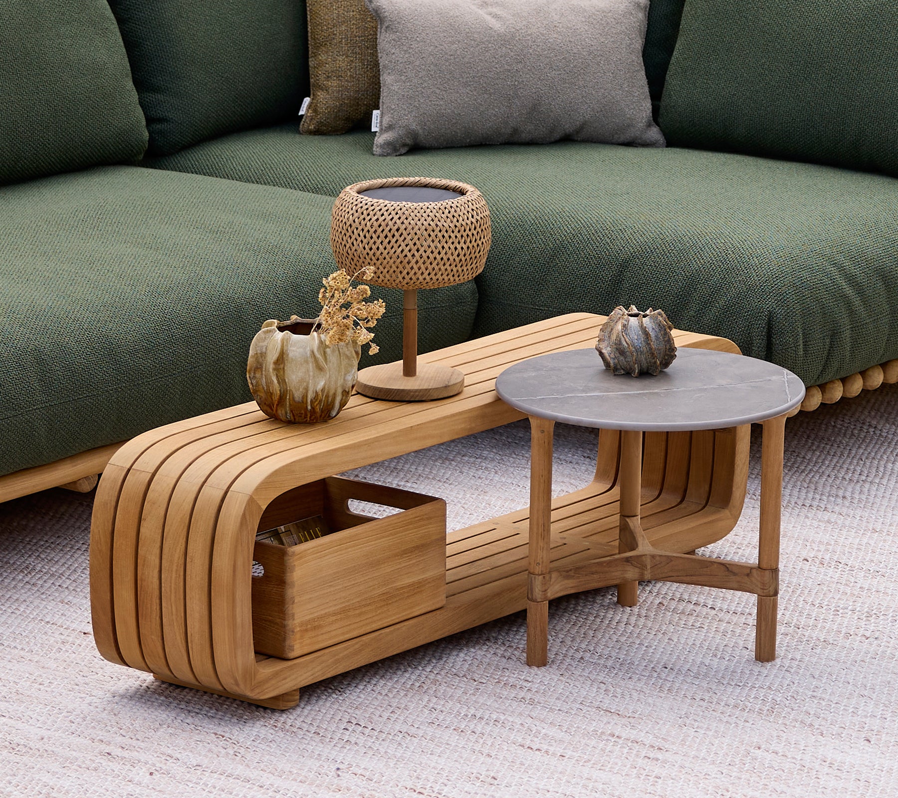 Modernes Holztisch mit einem grauen Beistelltisch, Lampe und dekorativer Vase in einer Lounge-Umgebung.