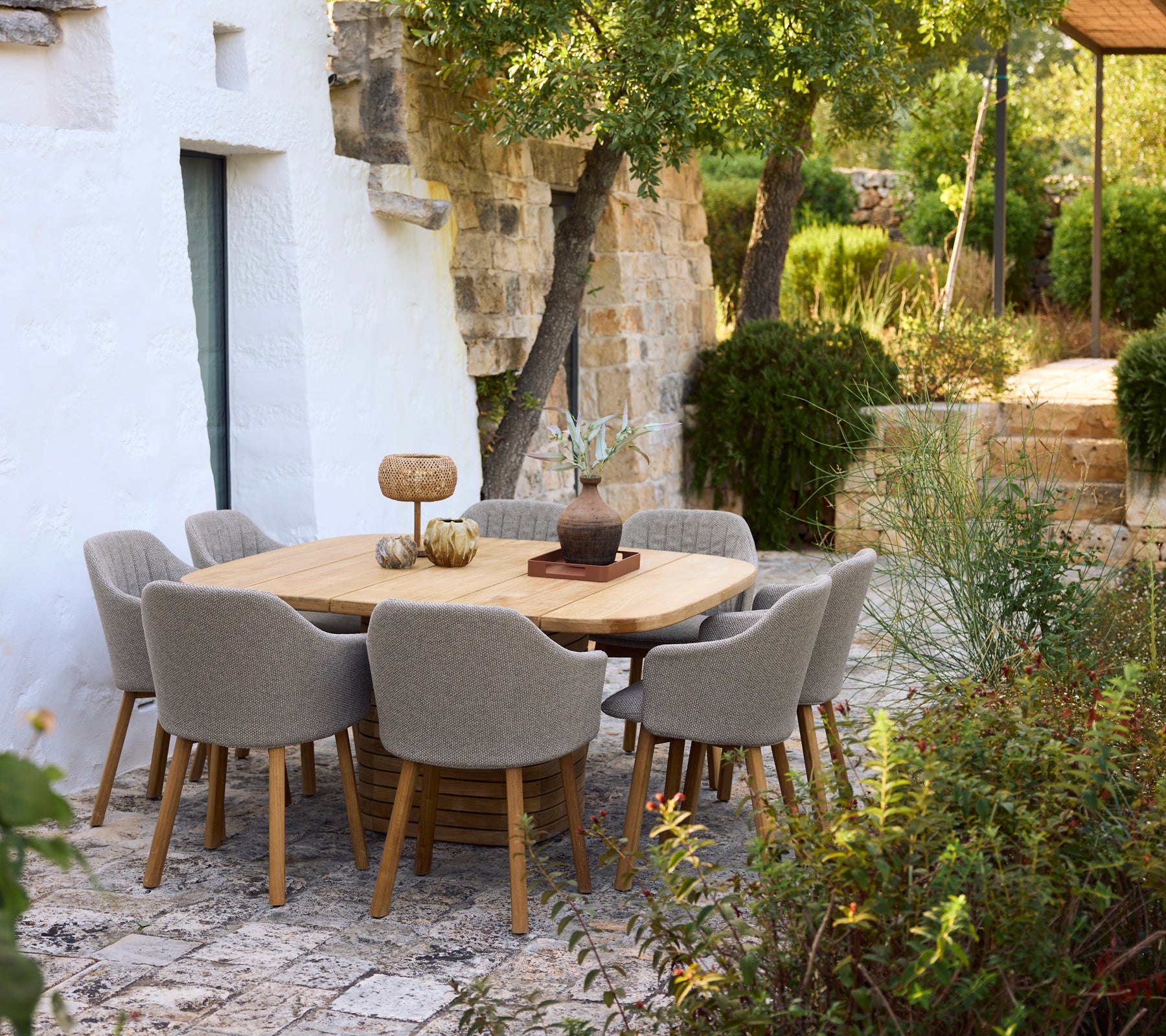 Moderner Holztisch umgeben von grauen Stühlen in einem Gartenambiente.