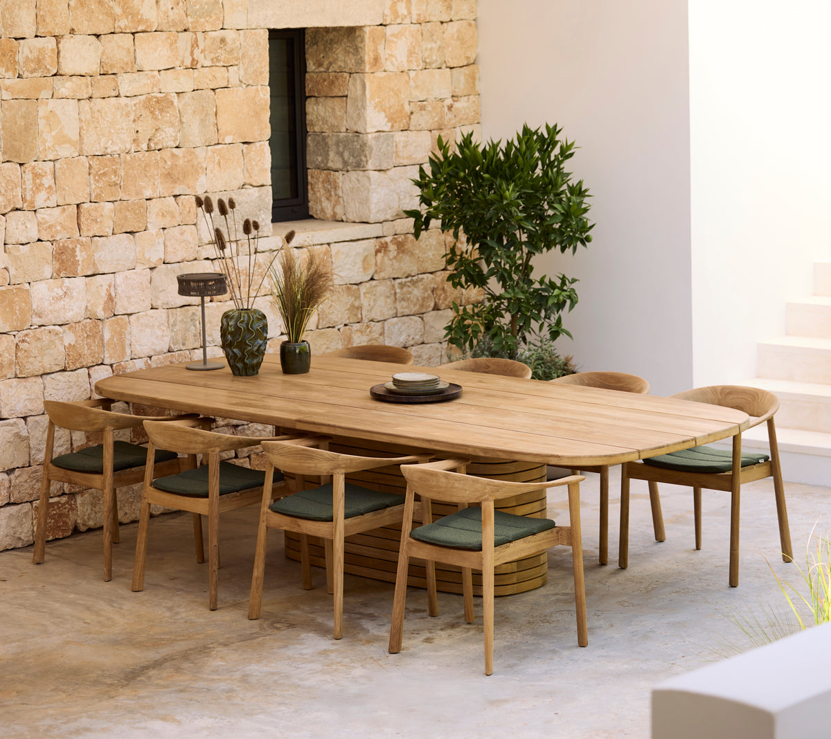 Modernes Holztisch mit grünen Kissen und Holzstühlen in einem minimalistischen Ambiente.